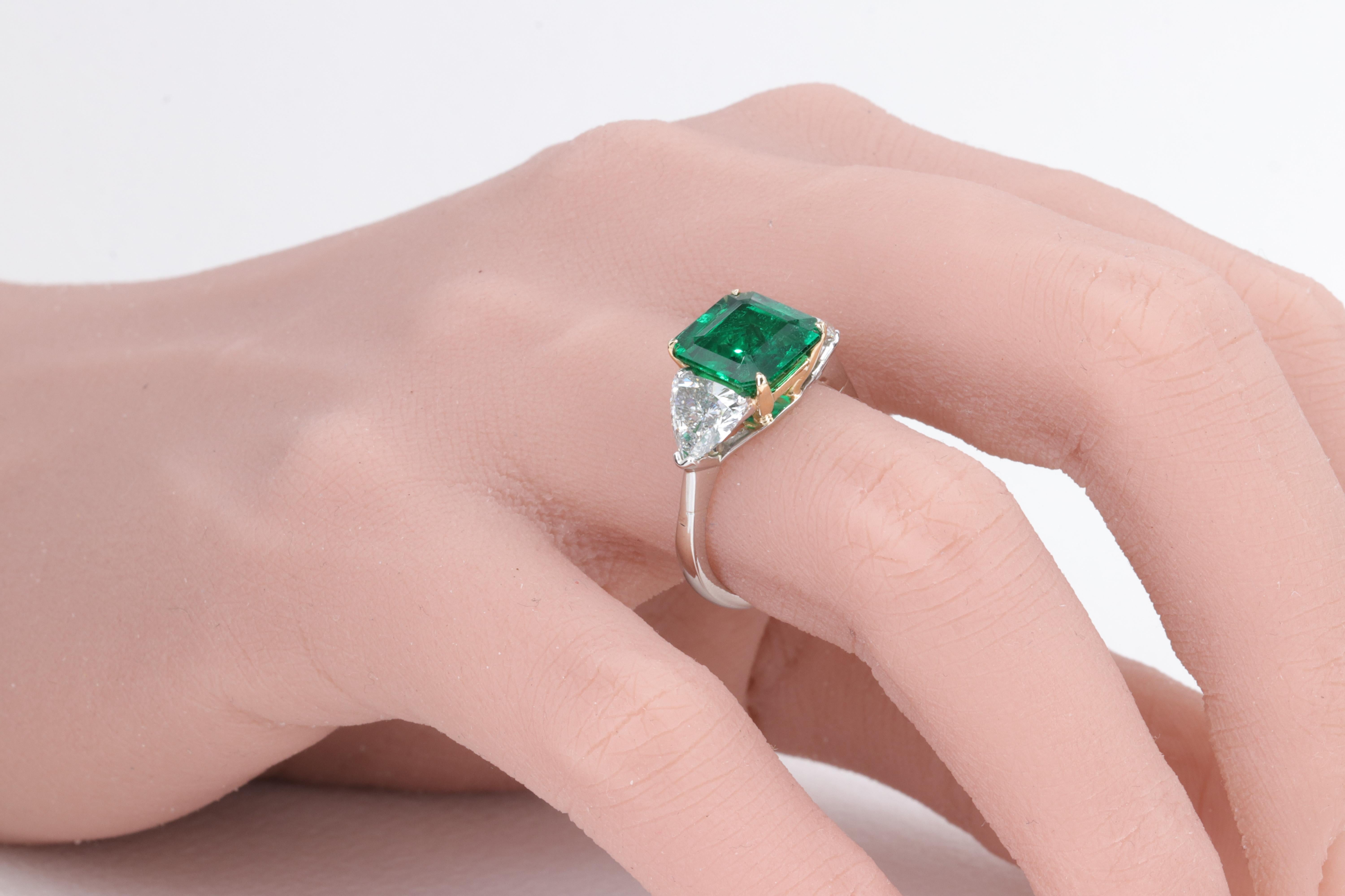 Hand fabricated platinum and 18 karat yellow gold three stone ring containing a 2.78ct Zambian Emerald with great clarity and exceptional vivid green color accompanied by and A.G.L. report set with two trillion cut diamonds weighing 1.55 carats in