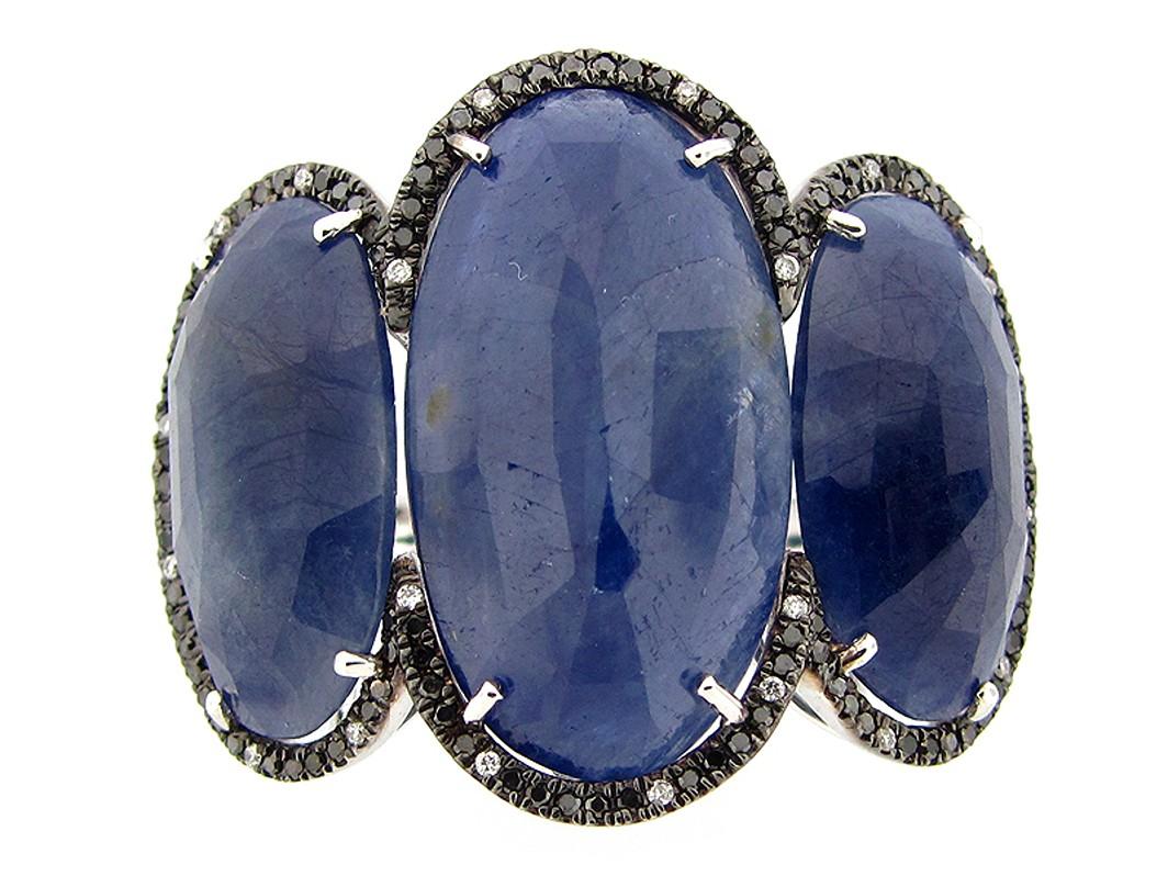 Cette magnifique bague de cocktail à trois pierres présente 3 saphirs ovales taille rose pesant au total 27,91 carats. Chaque saphir est entouré d'un halo de diamants ronds noirs et blancs, pour un total de 0,33 carat. 

Cette bague est sertie en or