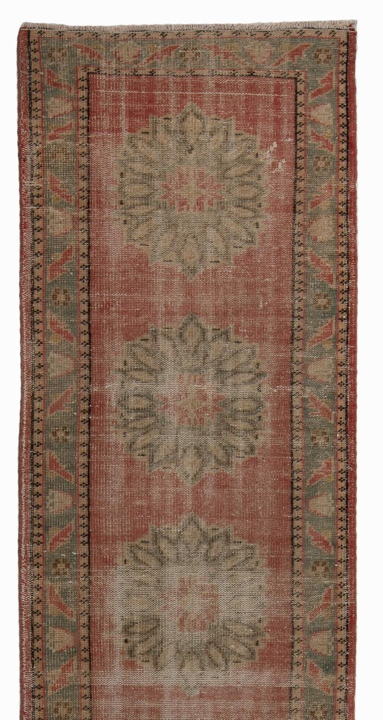 Vintage Turkish runner rug with floral-shaped multiple medallions in stone color across the length of the field against a plain background in faded red as well as a border in faded blue decorated with angular flower and leaf motifs. Size: 2.7 x 11.2