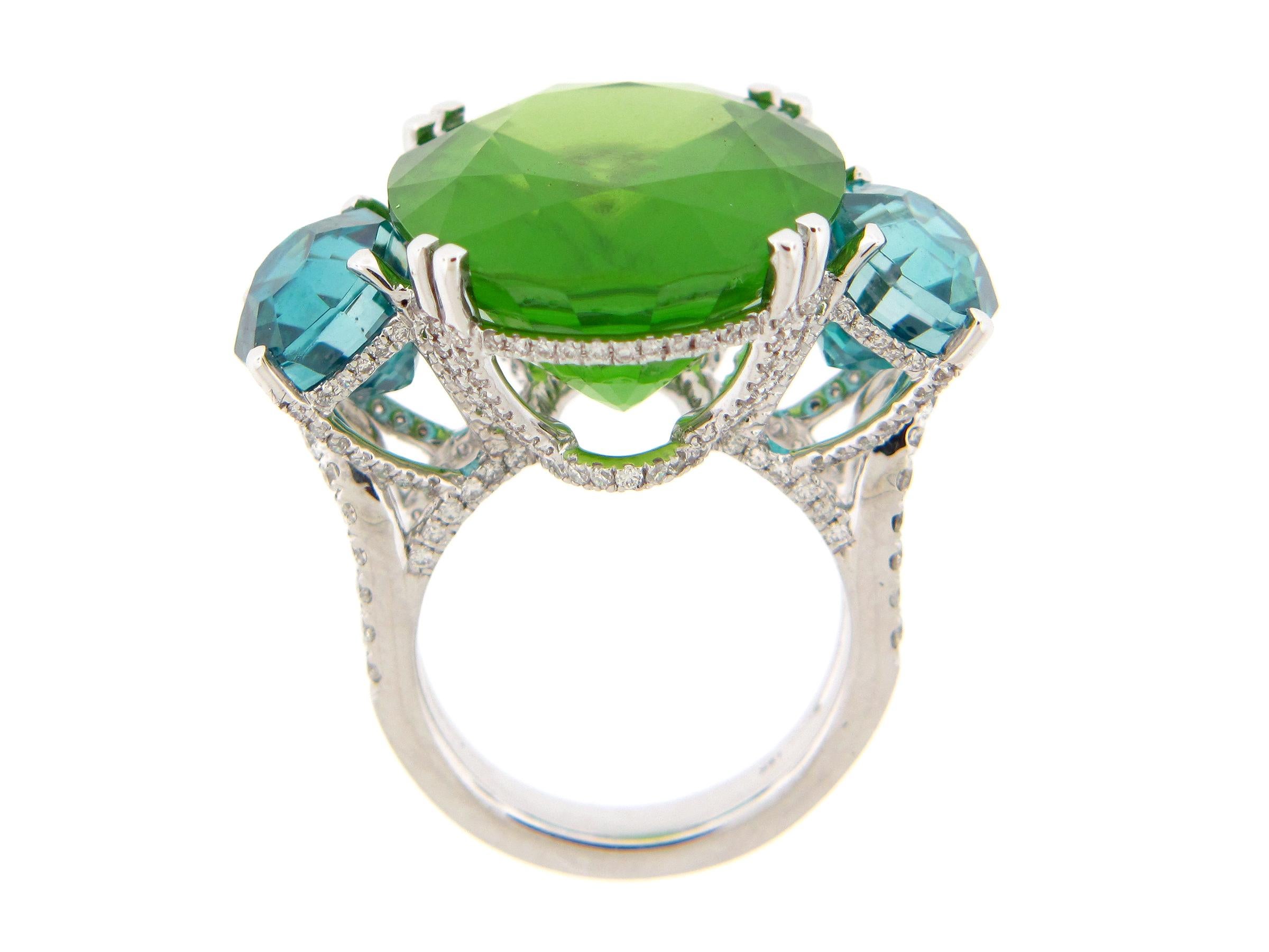 Cette superbe bague présente un péridot de Birmanie ovale vert de 28,10 carats, flanqué de deux zircons bleus de taille fantaisie (10,41 carats) maintenus dans une corbeille incrustée de diamants sur une double tige en diamant, le tout en or blanc