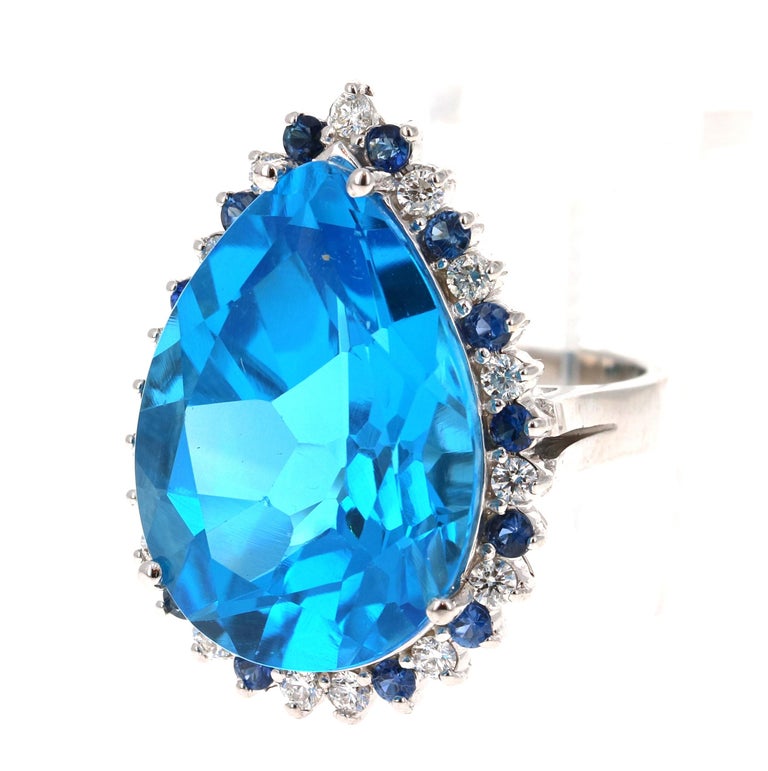 Beautiful to say the Least! This magnificent Pear Cut 27.09 Carat Blue Topaz is surrounded by 15 Round Cut Diamonds that weigh 0.53 Carats (Clarity: SI, Color: F) and 14 Blue Sapphires that weigh 0.60 Carats. The total carat weight of the ring is
