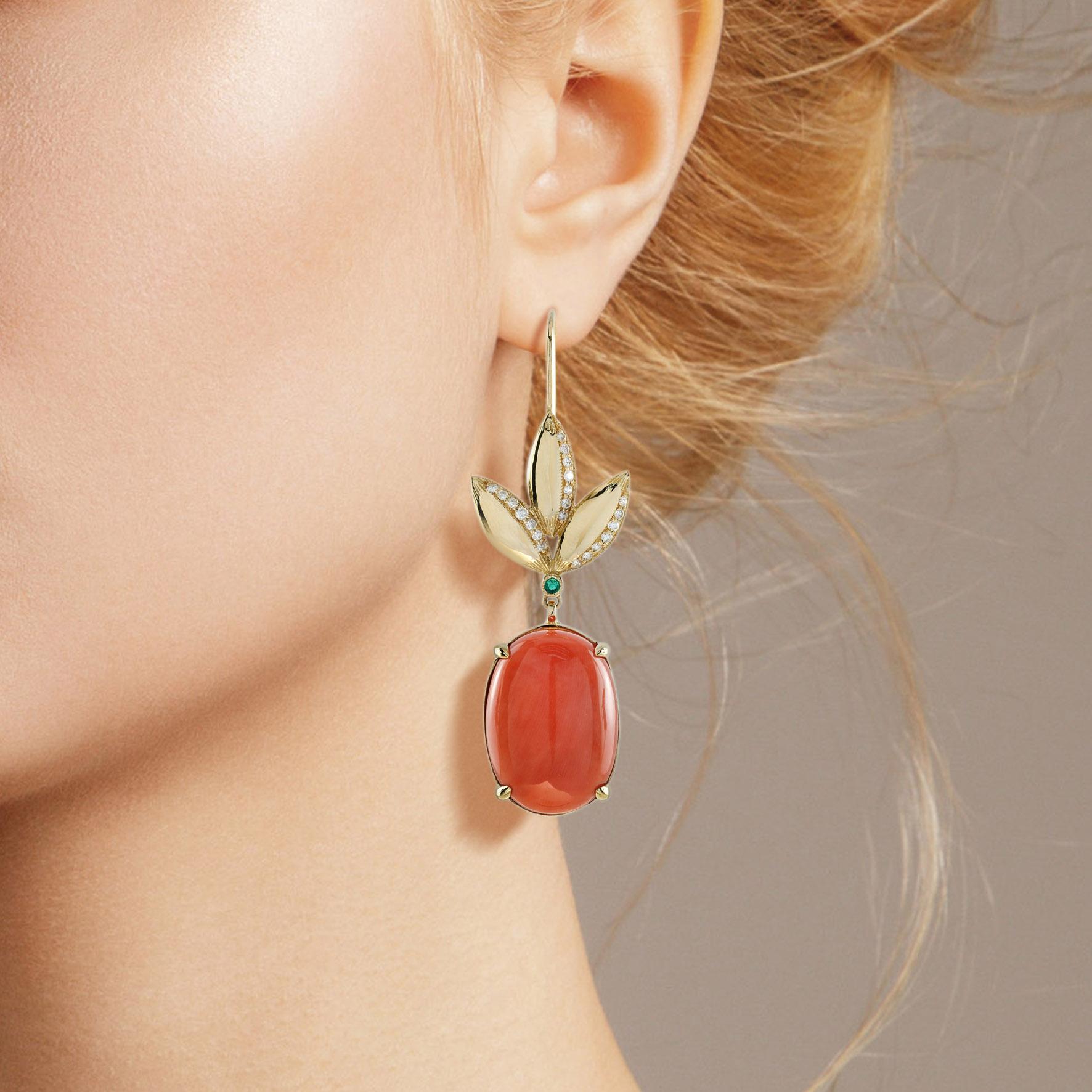 These one of a kind statement earrings are Vintage inspired handcrafted using approximately 28.40 carat oval shape corals. The upper part is decorated with tiny emerald hanging from leaves decorated with shimmering diamonds. Create your signature