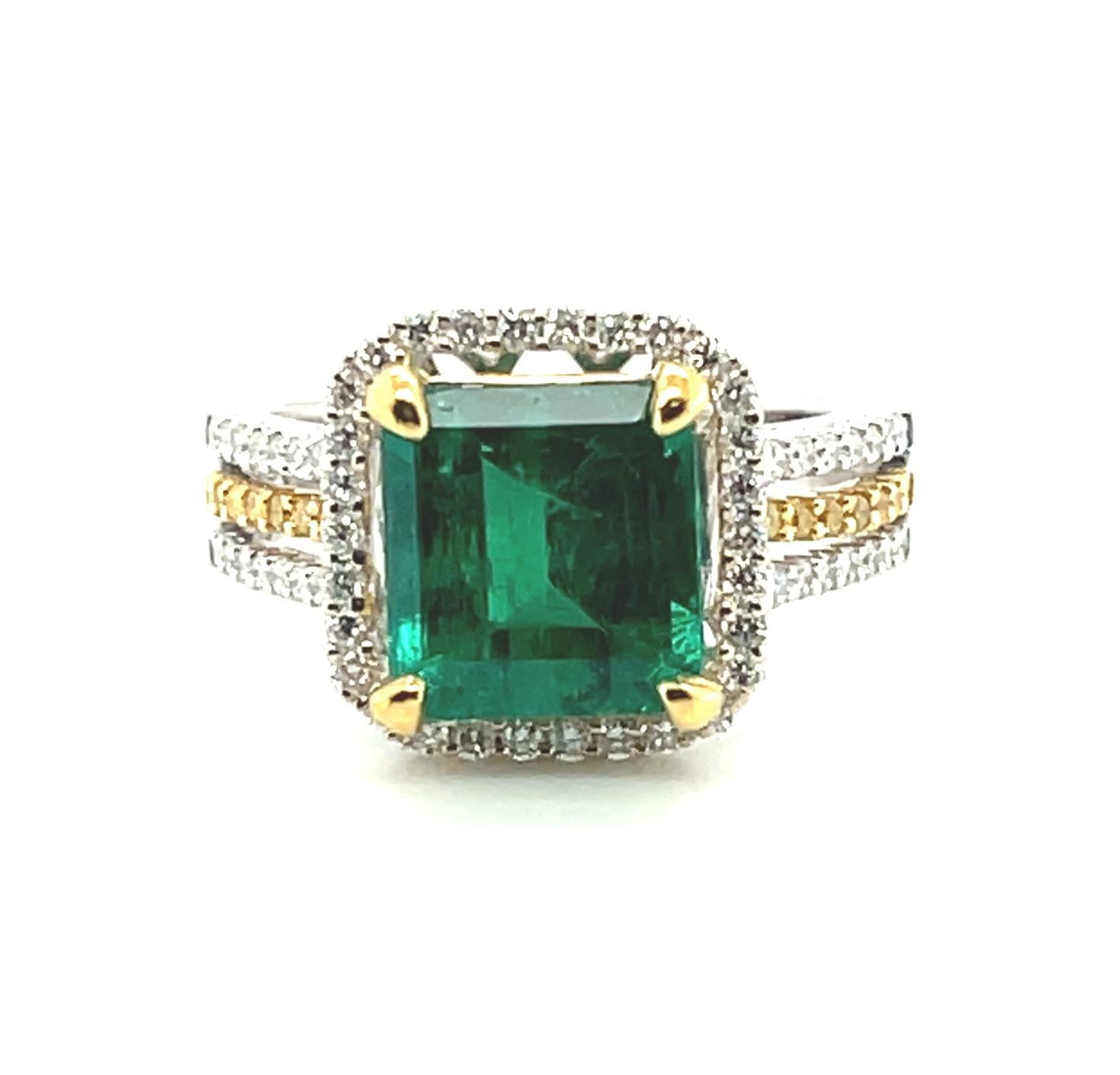 This beautiful cocktail ring features a deep, verdant green 2.85 carat emerald set in stunning 18k white and yellow gold. The center stone is framed by a halo of sparkling white diamonds and the band is set with both white diamonds and fancy, canary