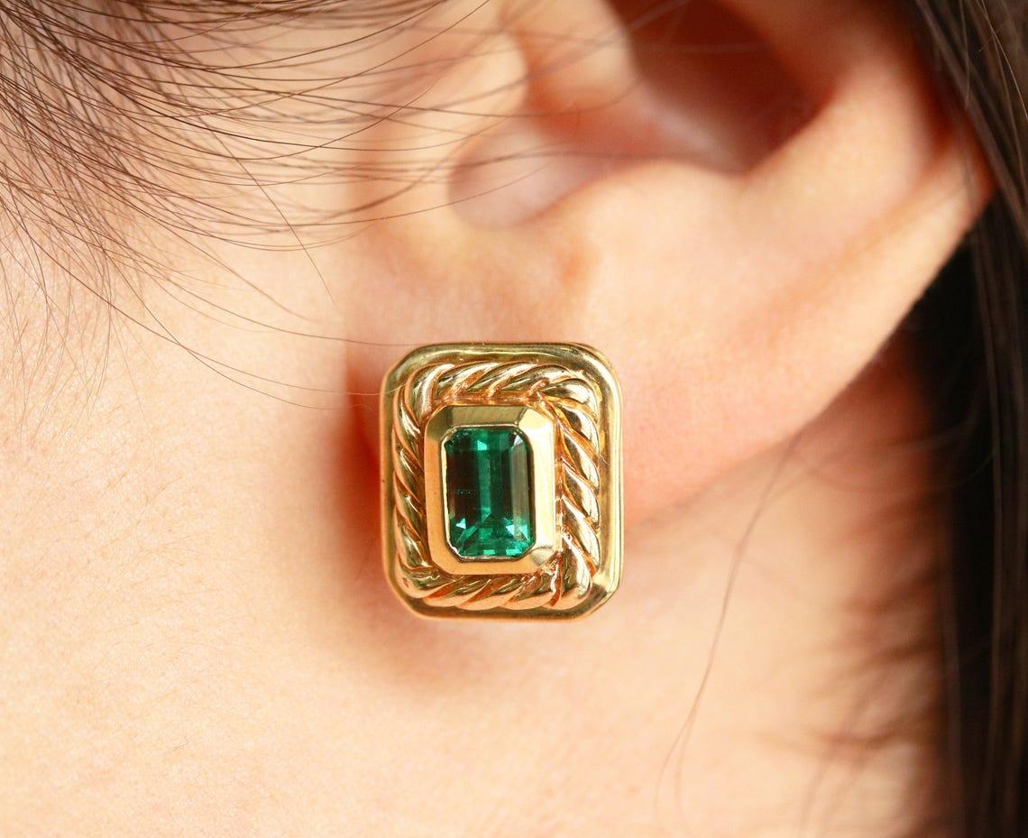 Displayed is a sleek pair of Colombian emerald and gold studded earrings. Fine-quality emeralds are the star piece for these gorgeous studs. Large 2.85tcw, earth-mined Muzo emeralds are hand-set and handmade in a solid 14K yellow gold setting. These
