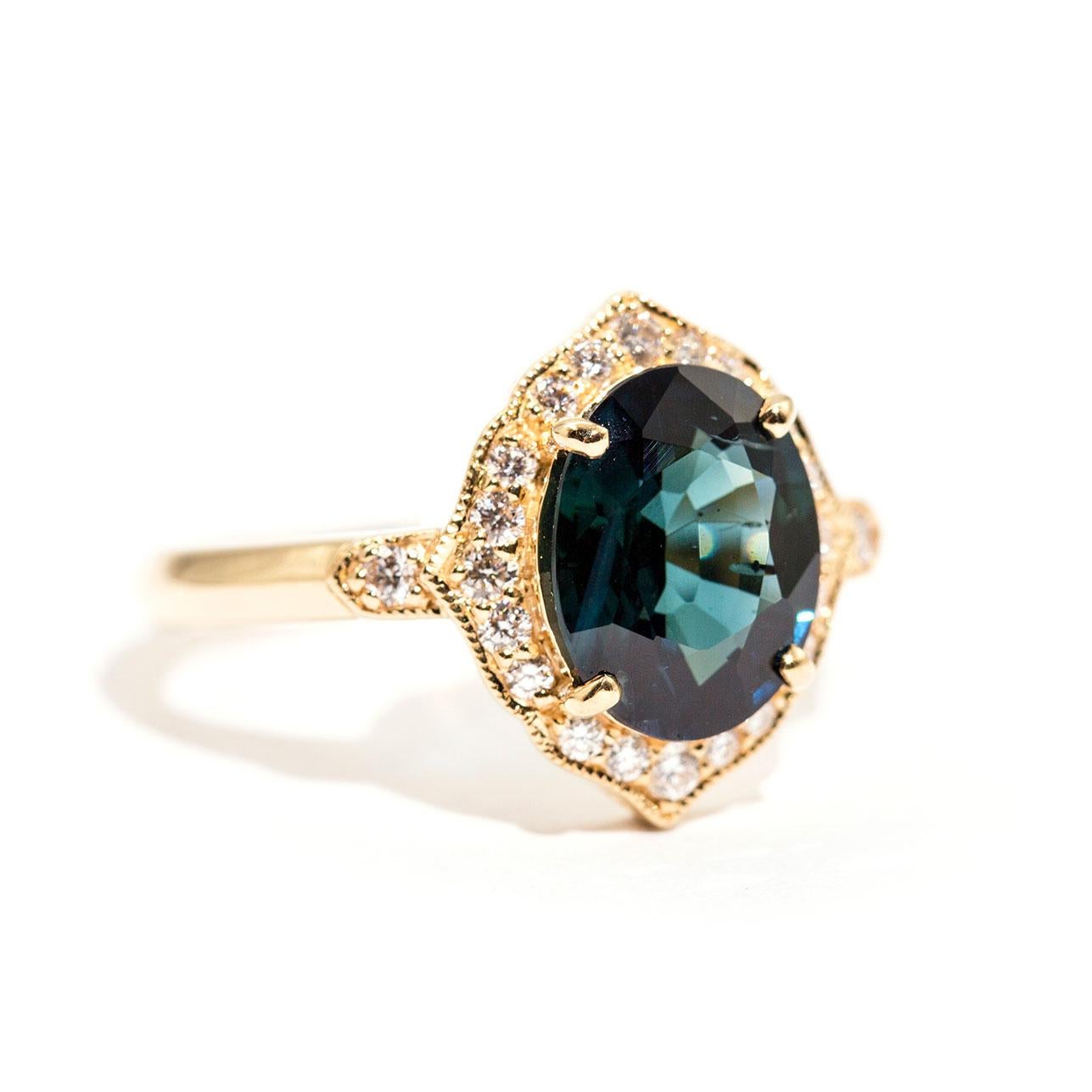 Forged in 18 carat yellow gold is this gorgeous ring that features the most lovely 2.87 carat oval cut natural sapphire of an alluring deep teal colour, with flashes of deep blue, and is encompassed with a sparkling border of round brilliant cut