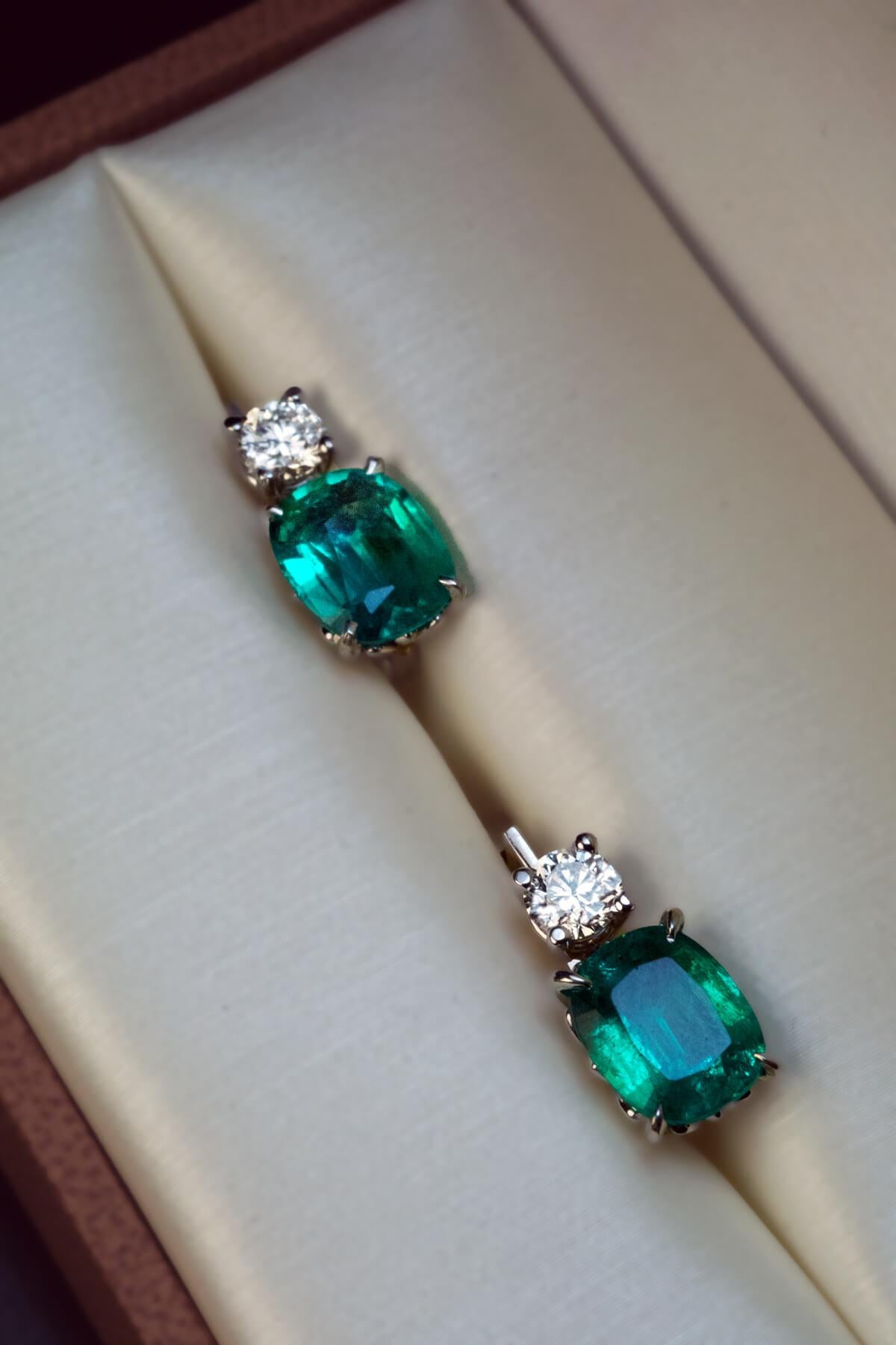 These 14K white gold contemporary earrings feature two cushion cut emeralds of vivid bluish green color. The emeralds (8.5 x 6.9 mm and 7 x 8.6 mm) are accented by two bright white brilliant cut diamonds (F-G color, VS2-SI1 clarity).  Total emerald