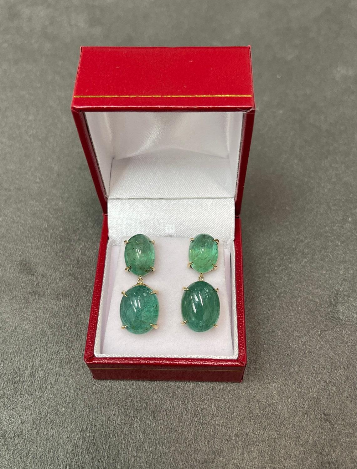 Large statement size Emerald dangling studs in fine 14K yellow gold. Displayed are medium-green oval cut emeralds with very good transparency, accented by a simple four-prong gold mount, allowing for the emeralds to be shown in full view. The
