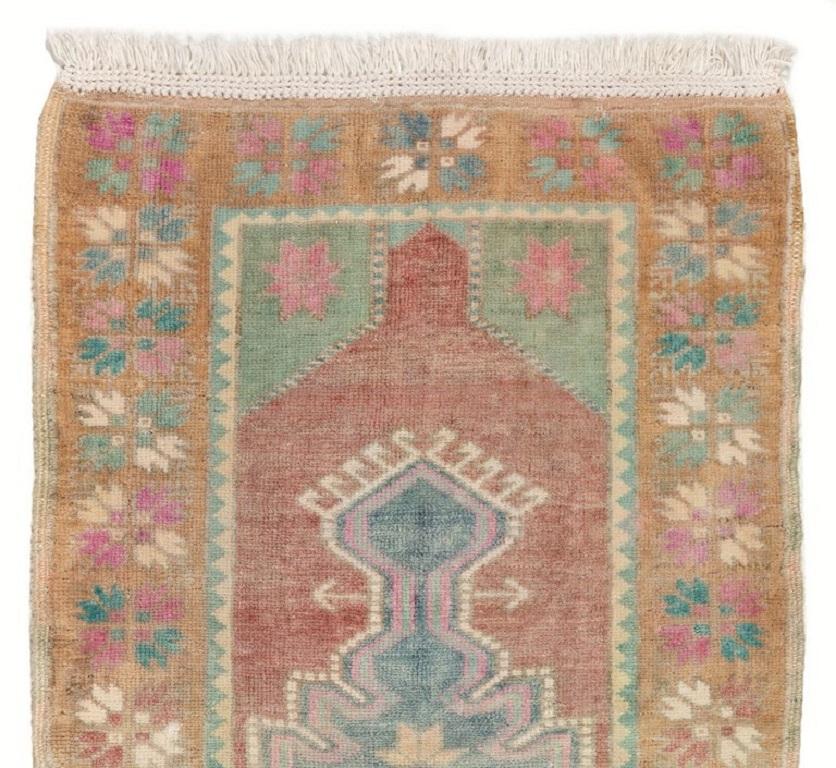 This vintage hand-knotted Turkish rug has soft wool pile and is in very good condition. It features a geometric design with a large medallion at its center. Its colors, including camel, madder red, navy blue, pink, mint green and cream, have a soft