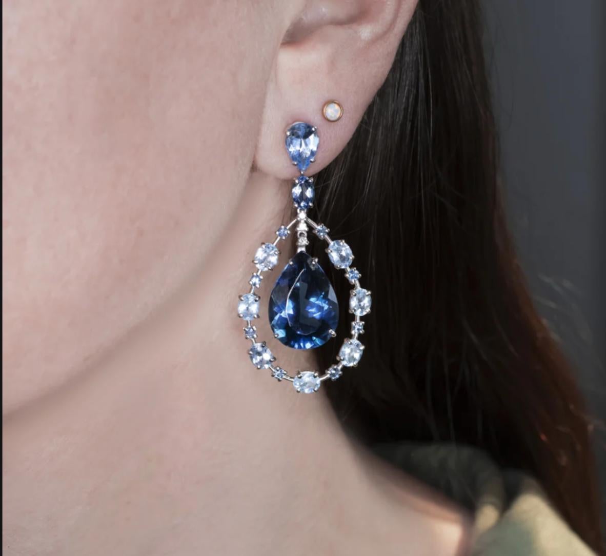 Bold, elegant, and full of color, these dramatic dangle earrings feature a striking 29 carats of topaz in rich blue hues. At the center, a pair of vivid 20 carat London blue pear-shaped topaz stones take the spotlight, surrounded by an artistic halo