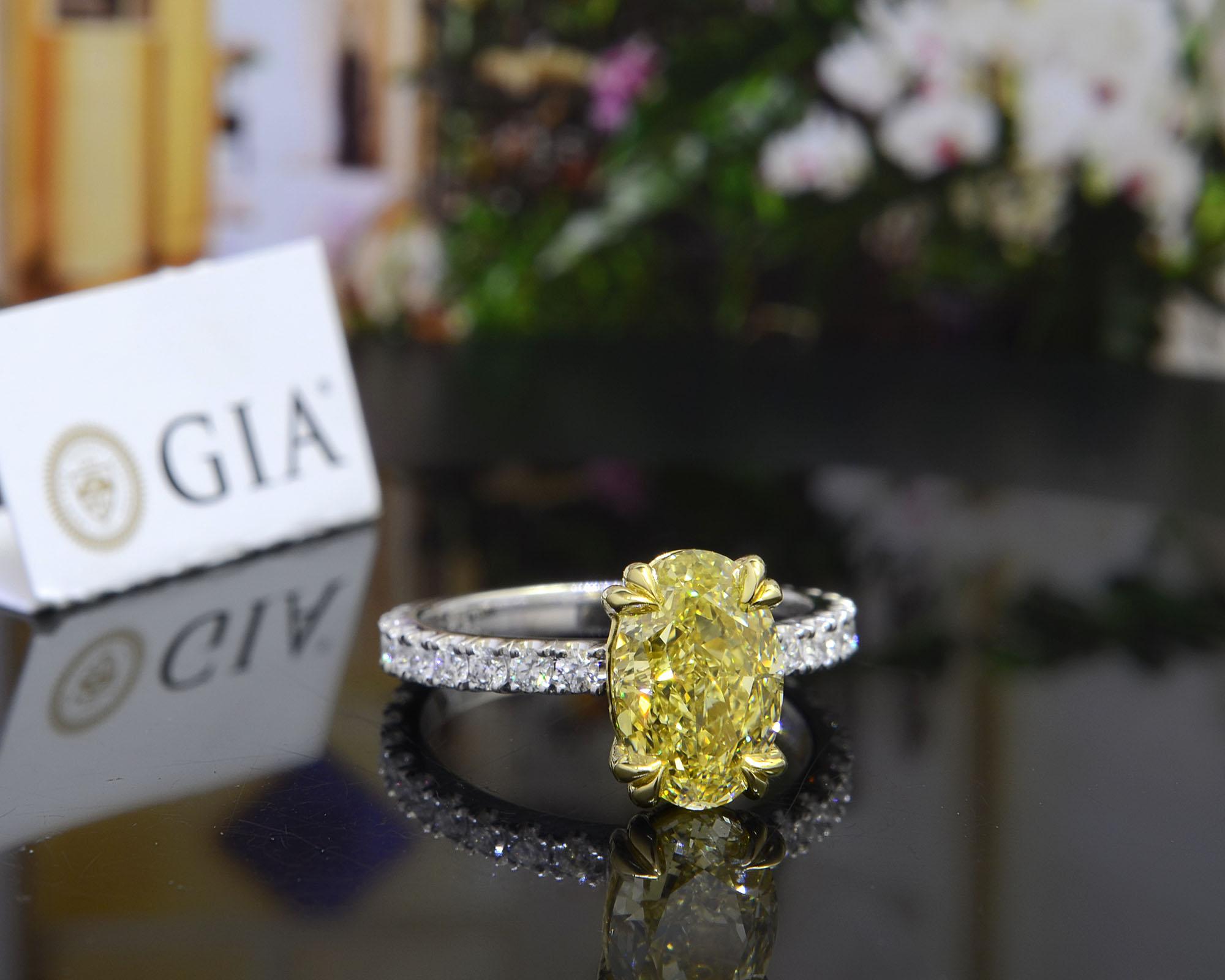 Cette ravissante bague de fiançailles en diamant canari est ornée d'un diamant ovale de 2,20 ct. de couleur naturelle jaune de fantaisie et de pureté VVS1. Autour de la pierre centrale et tout autour de la tige, 0,70 ct. de diamants ronds sont