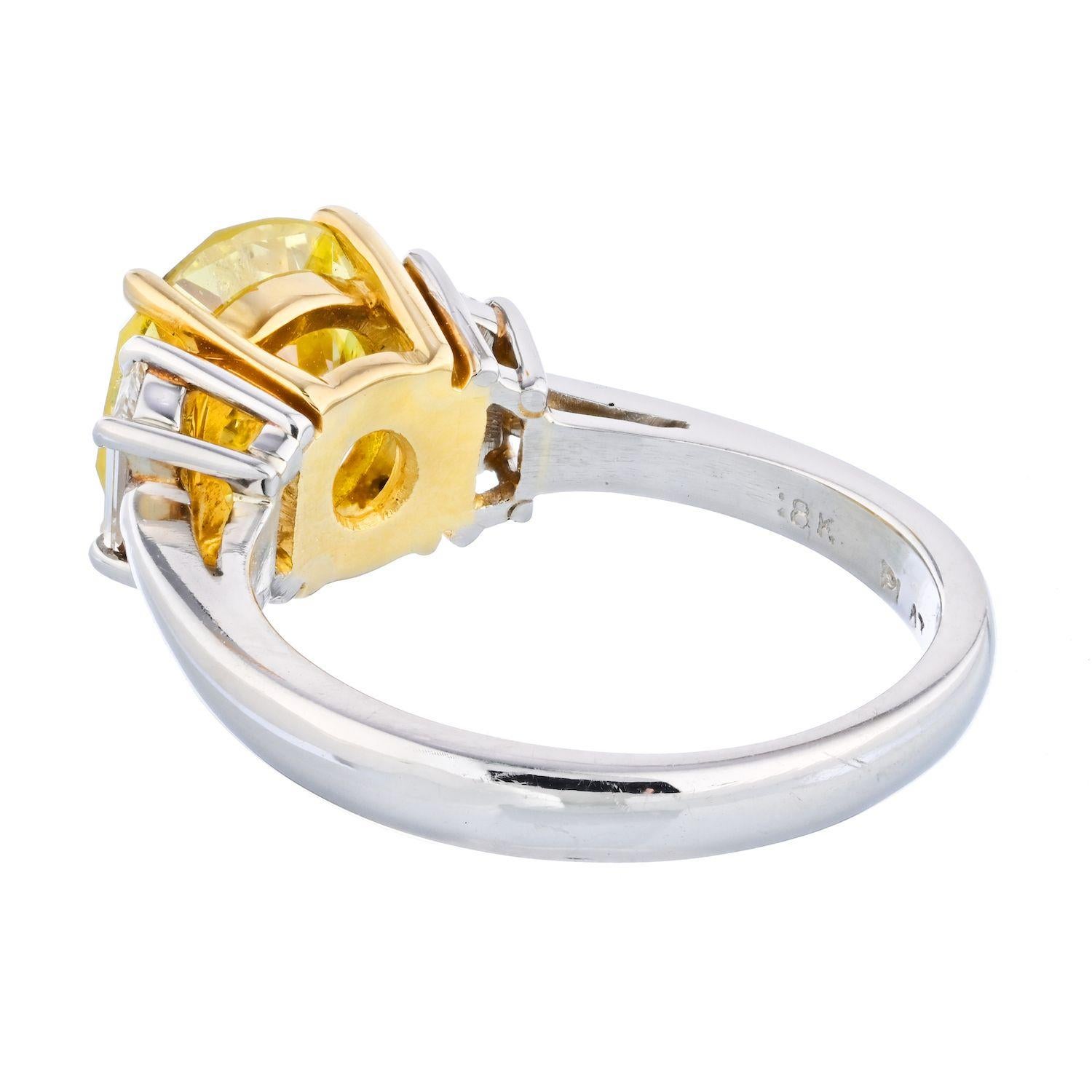 This is a very unique three stone diamond engagement ring crafted in Platinum and 18k yellow gold mounted with a fine round brilliant cut diamond: it is a 2.90 carat round brilliant cut that is graded by GIA as a Fancy Intense Yellow. It is flanked
