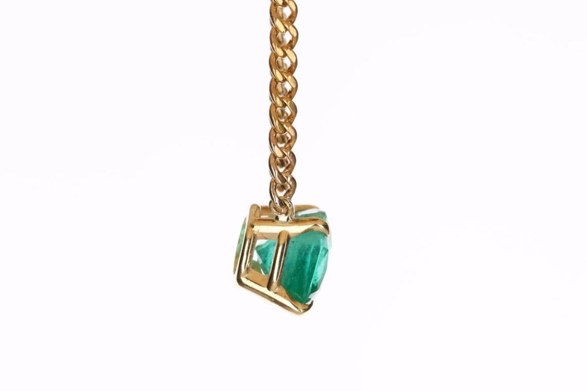 Displayed is an East to West emerald solitaire necklace. This gorgeous solitaire ring carries a cushion-cut emerald in a four-prong setting. Fully faceted, this gemstone showcases excellent shine. The emerald has excellent clarity with minor flaws