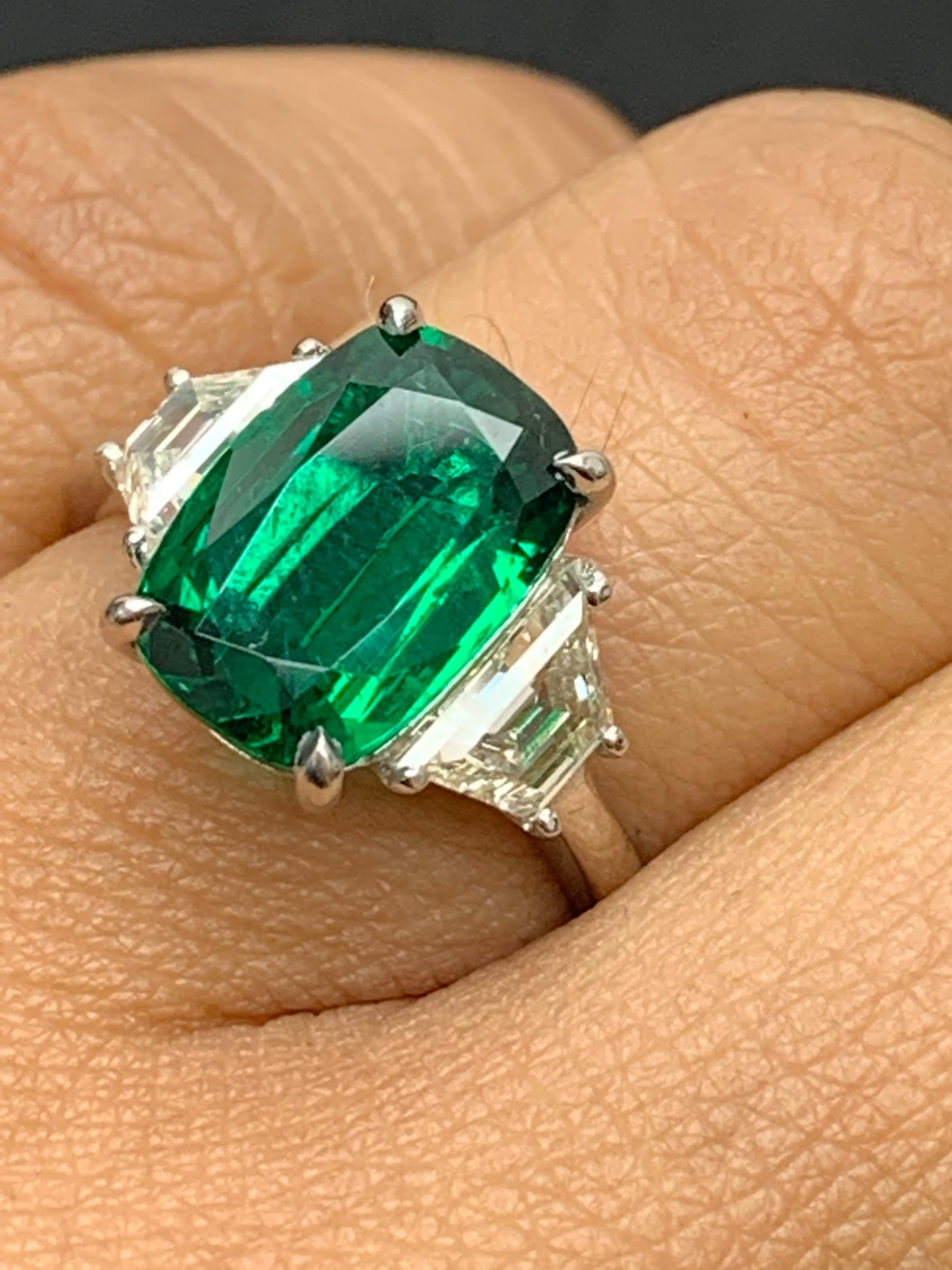Showcases an elongated Cushion cut, Vibrant color Emerald weighing 2.91 carats, flanked by two brilliant cut trapezoid diamonds weighing 1.05 carats total. Elegantly set in a polished platinum composition.