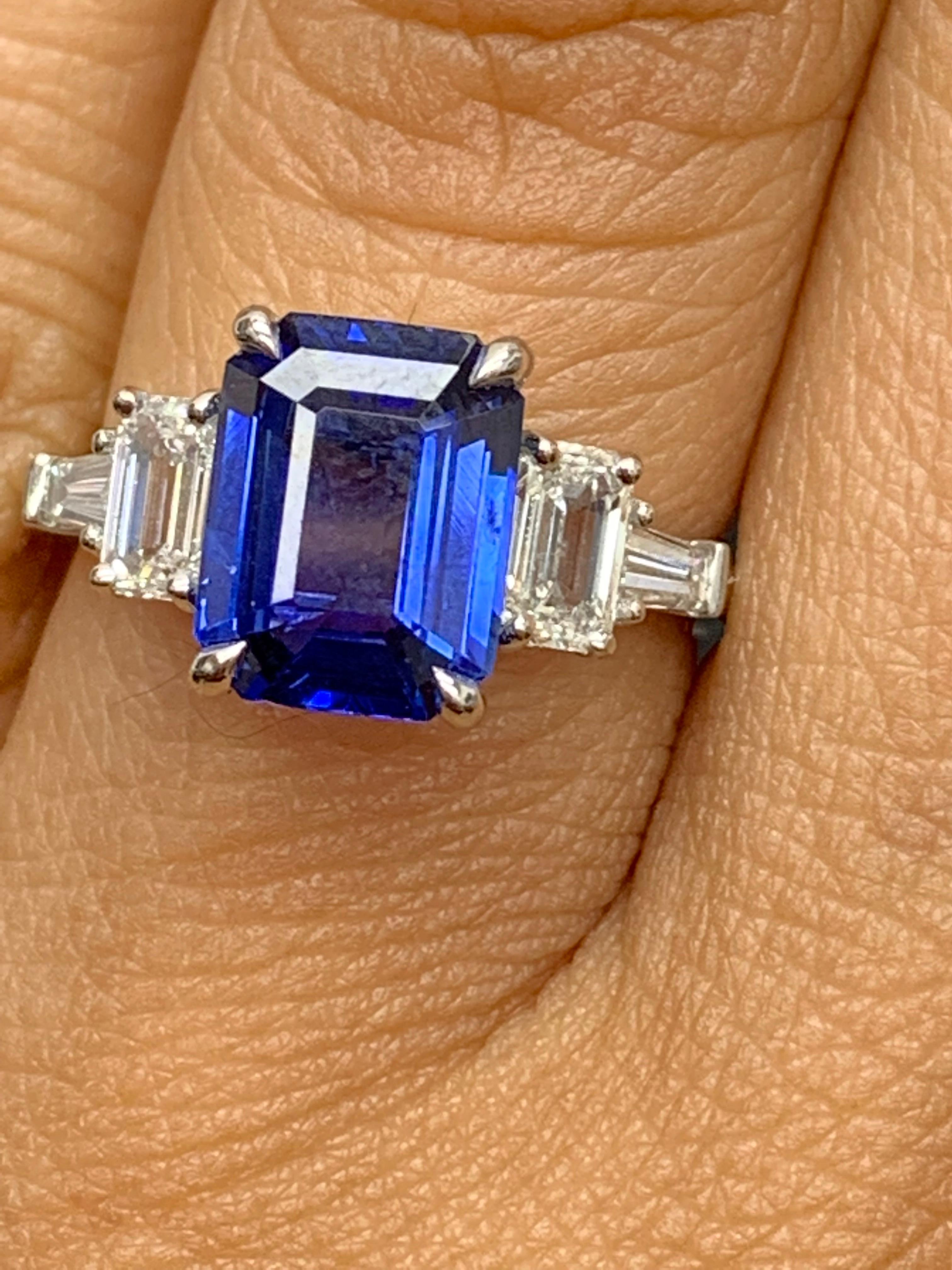 A stunning ring showcasing a rich intense emerald cut blue sapphire weighing 2.91 carats.  Flanking the center stone are two emerald-cut diamonds weighing 0.68 carats and two baguette diamonds on each side weighing 0.25 carats in total, Made in
