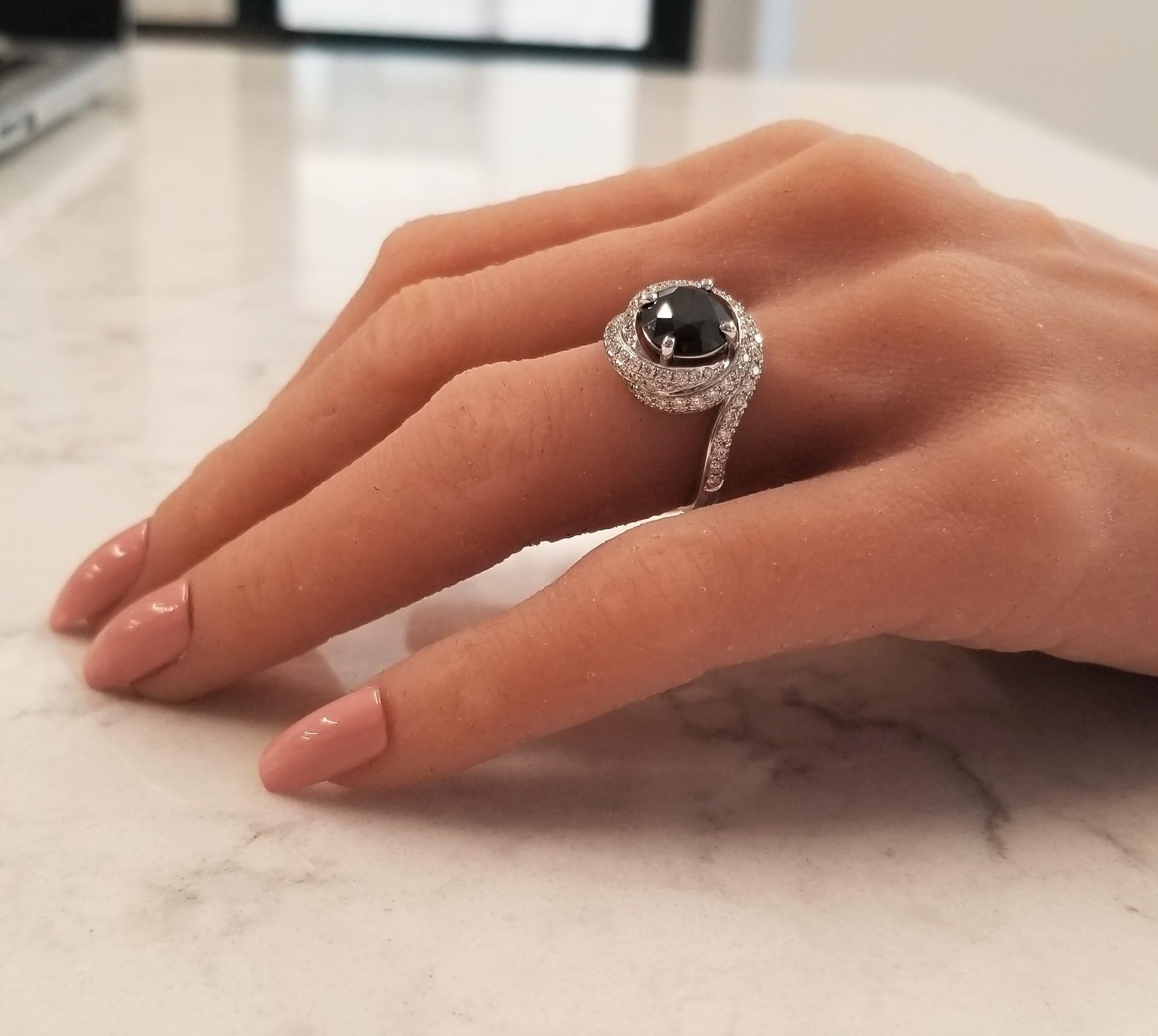 This is a picture perfect black and white combination like the keys on a Steinway piano. This ring features a 2.92 carat round black diamond. It measures 8.8mm. Its color is evenly distributed with excellent luster. The black diamond is swirled with