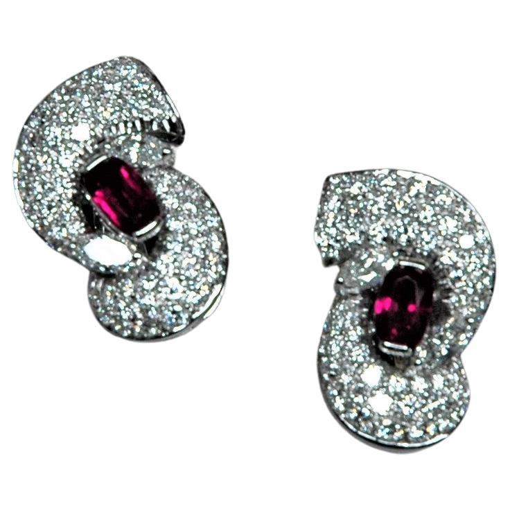 Magnifiques boucles d'oreilles en or blanc ornées de diamants et de rubis. Leur forme rappelle une étreinte, réalisée avec un magnifique pavé de diamants. Au centre, un rubis ovale et deux diamants taille navette.