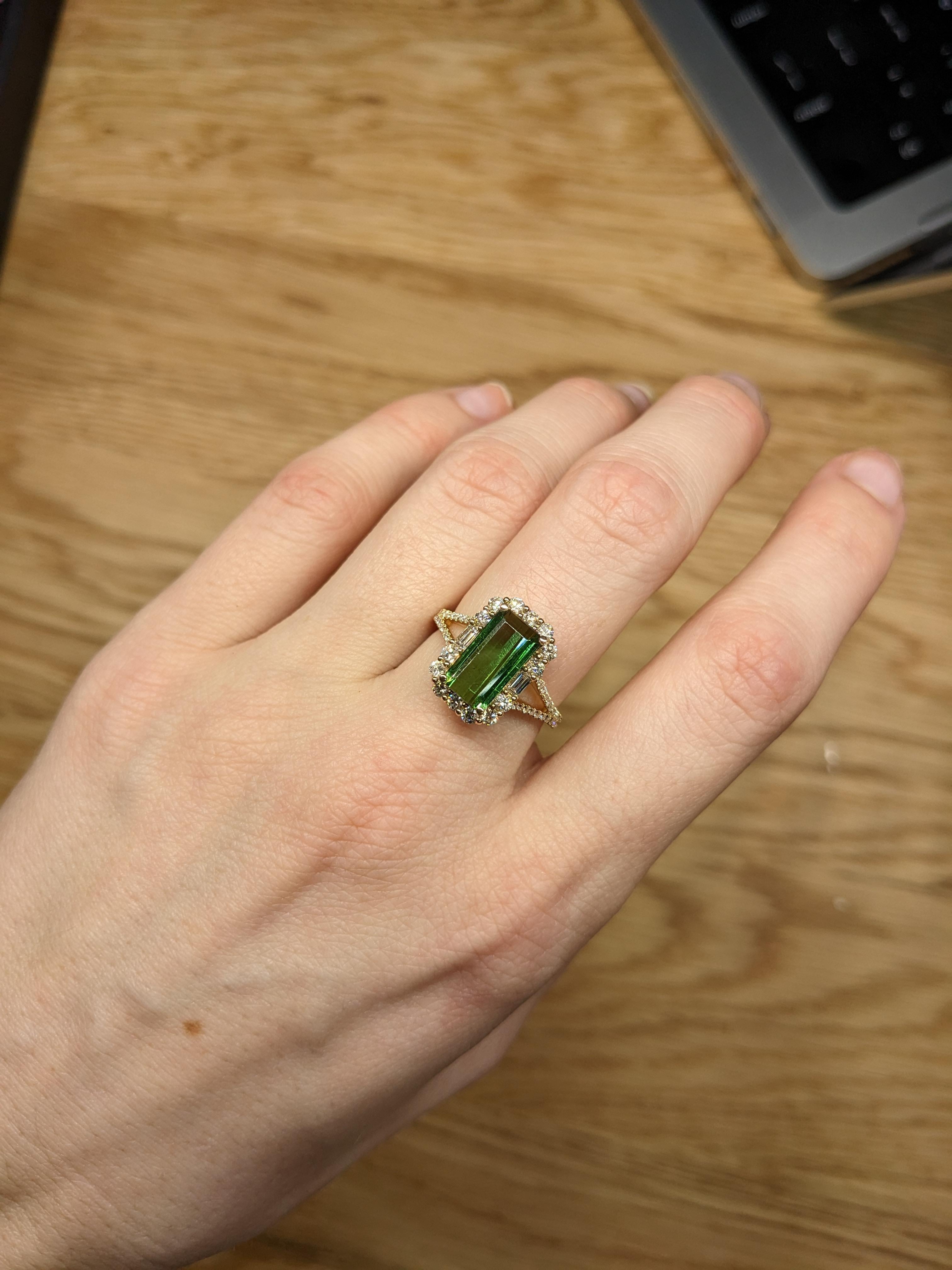 A beautiful engagement ring made with 14K yellow gold. The centerpiece of the ring features a 2.93-carat chrome tourmaline gemstone in an emerald cut, measuring 11x6mm. Surrounding the tourmaline are diamond accents, adding an elegant touch to the