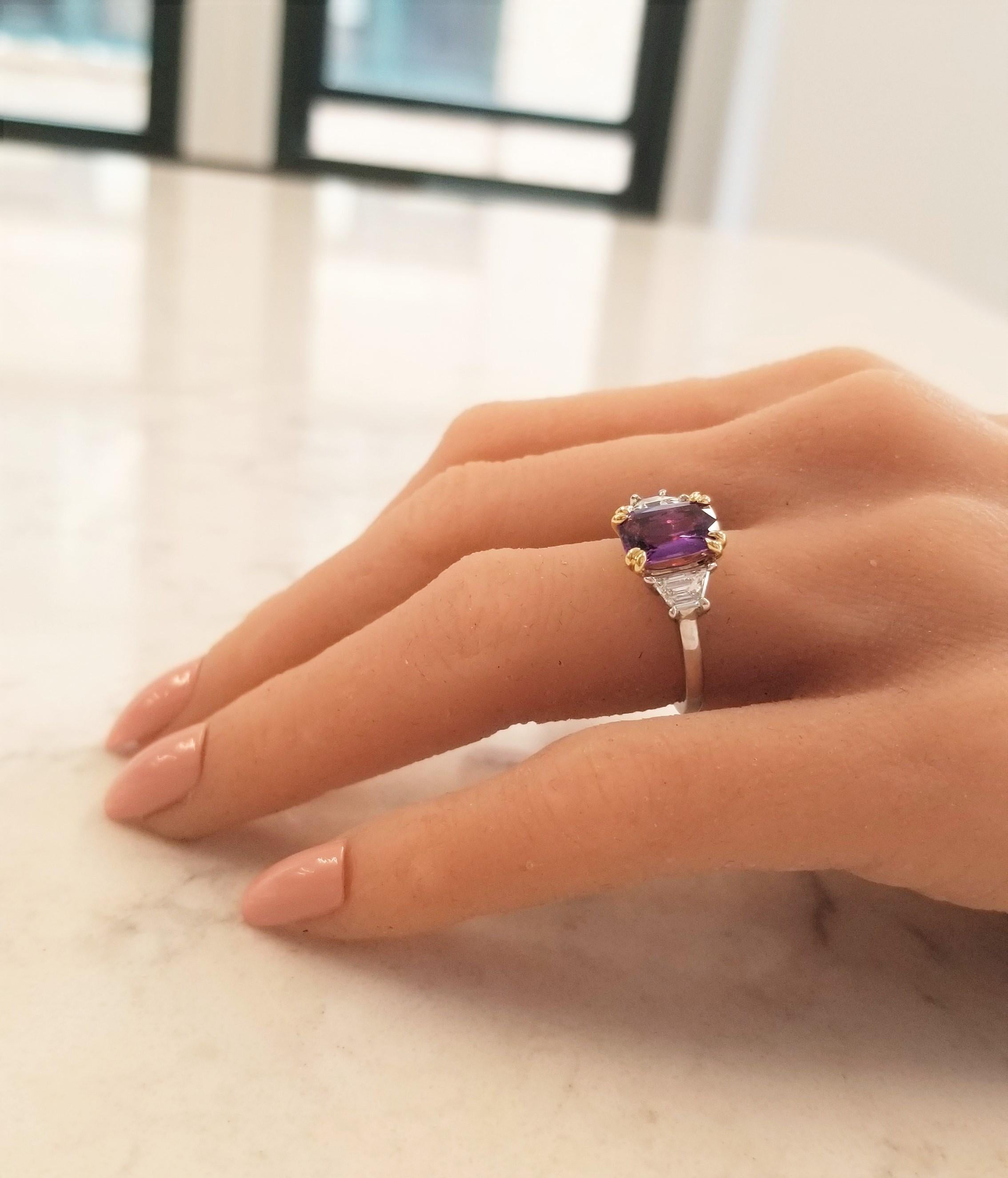 This luxurious three-stone statement ring features a scarce purple sapphire emerald cut that measures 9.70x7.19x4.20MM and weighs 2.98 carats. The gem source is Sri Lanka; its color is vivid purple. The transparency and luster are excellent. In