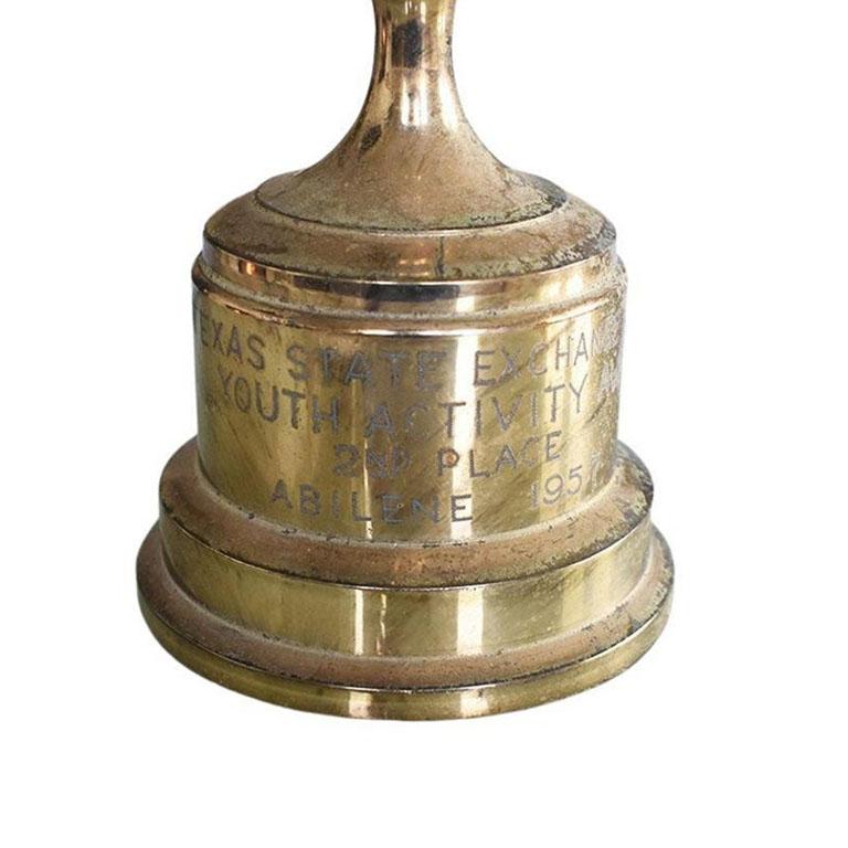 A tall brass metal trophy from the Texas State Exchange Clubs. This Trophy features a figural woman with wings atop a trophy cup with handles. She holds a flam into the air high above her head. The base is round, and reads:

Texas State Exchange