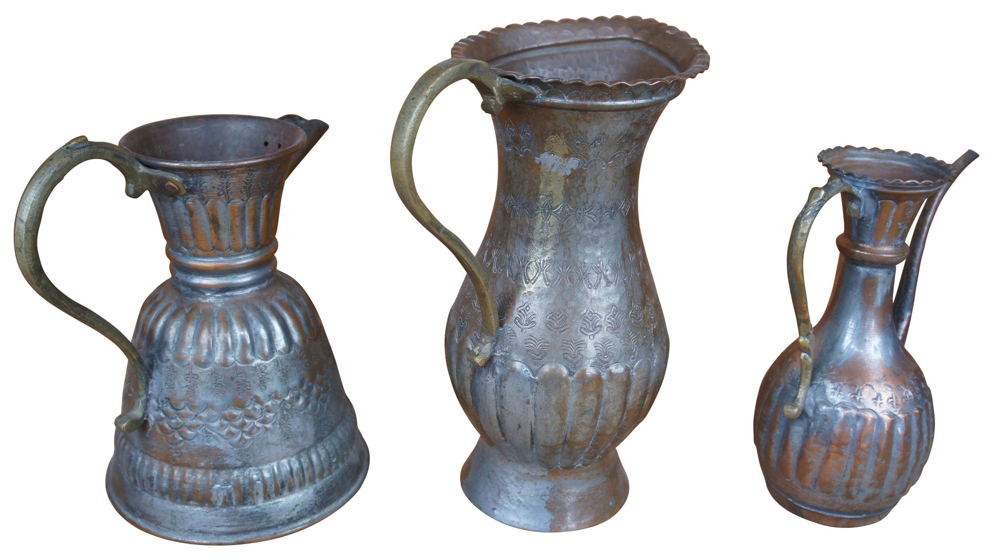 Three of assorted hammered copper pitchers featuring various designs and styles with fleur de lis and ribbed accents, and scrolled handles. One features a bonsai gooseneck spout. Stamped with ‘Egypt’ on the bottom.

tallest- 9