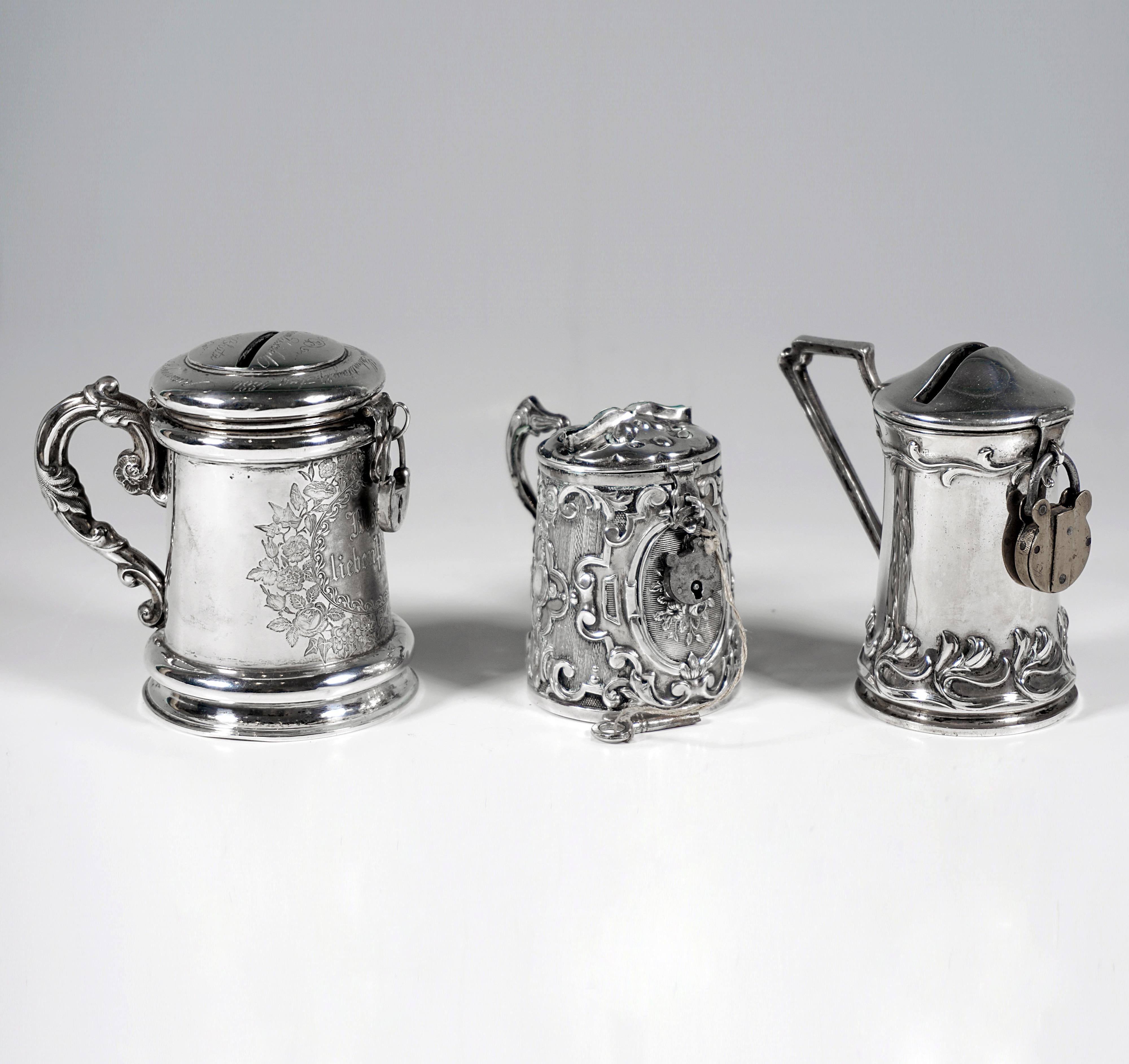 Three silver money boxes in the shape of a tankard, handle, hinged lid, all boxes with locks, 1 key present.

Dating:           19th Century
Material:         Silver '800' & 13 Lot ('812.5')
Total weight:  ca 230 grams / 8.09 oz / 7.39 troy