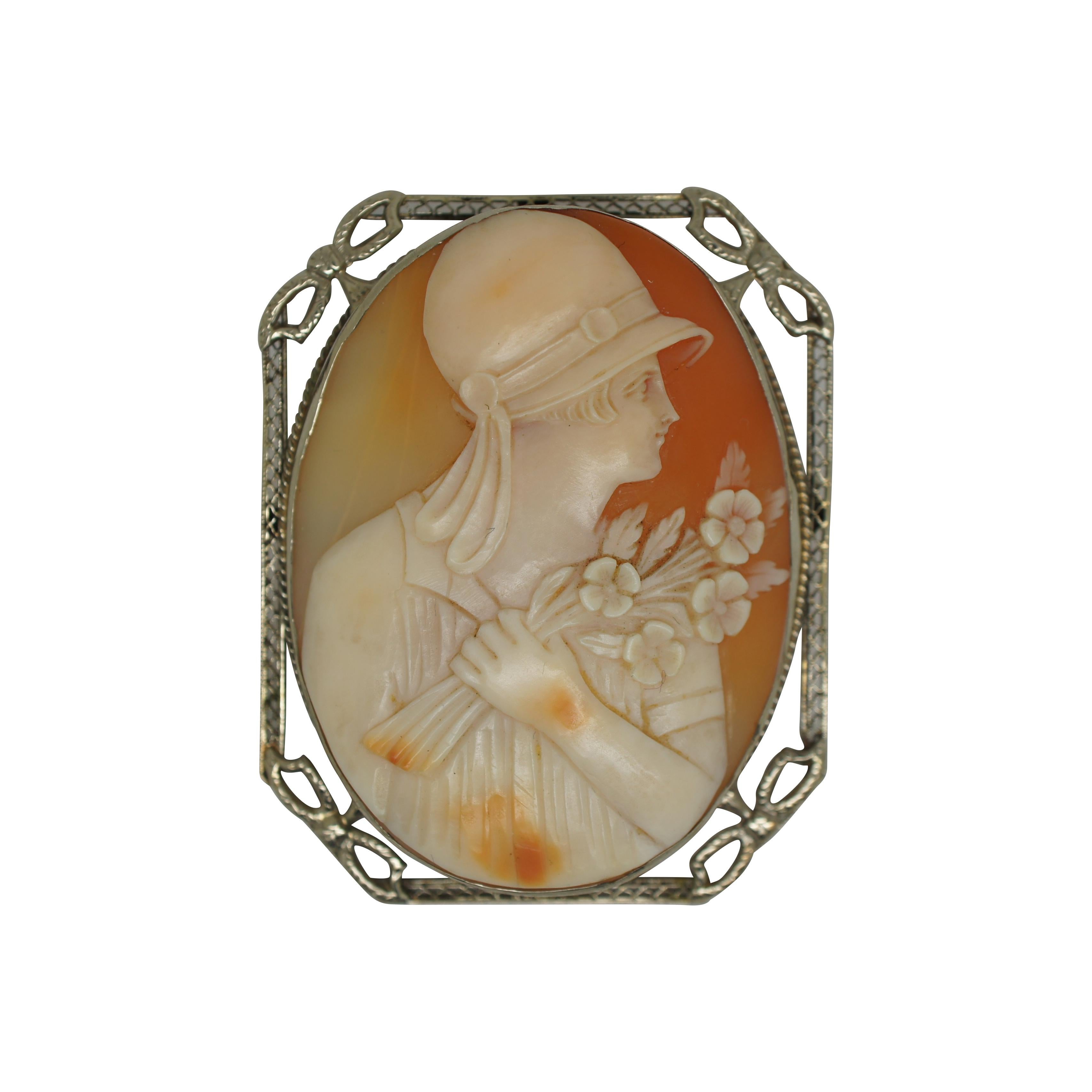 Lot of three antique late 19th to early 20th century hand carved shell cameos. Stunning large 14k gold oval cameo showing a woman in flapper / 1920’s attire holding a bouquet of flowers, set in a rectangular frame with filigree and bow shaped