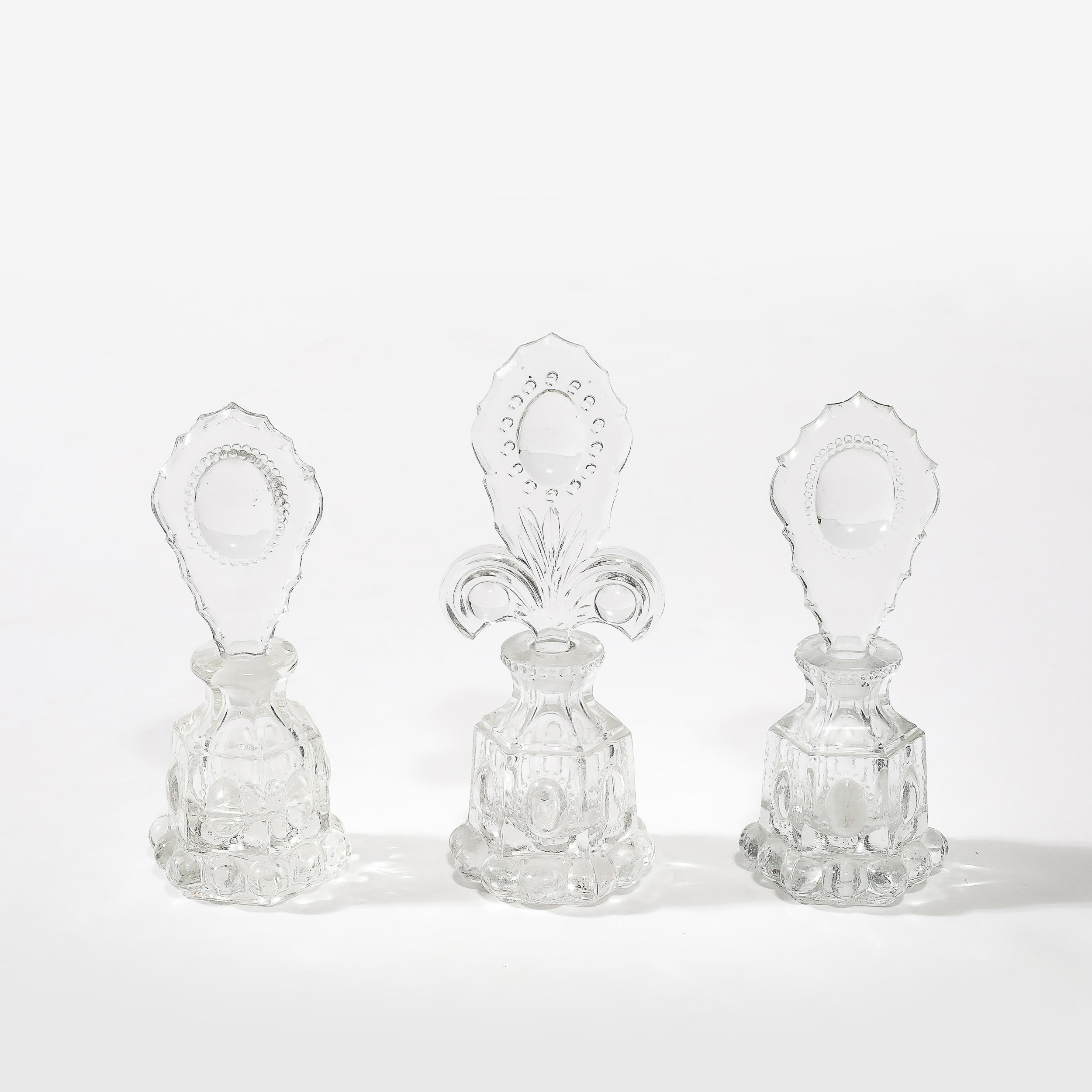 This stunning set of three Art Deco pressed glass perfume holders epitomizes the elegance and innovation of 1930s American design. Each bottle features meticulous hobnob detailing along the body, creating a striking textured finish that reflects