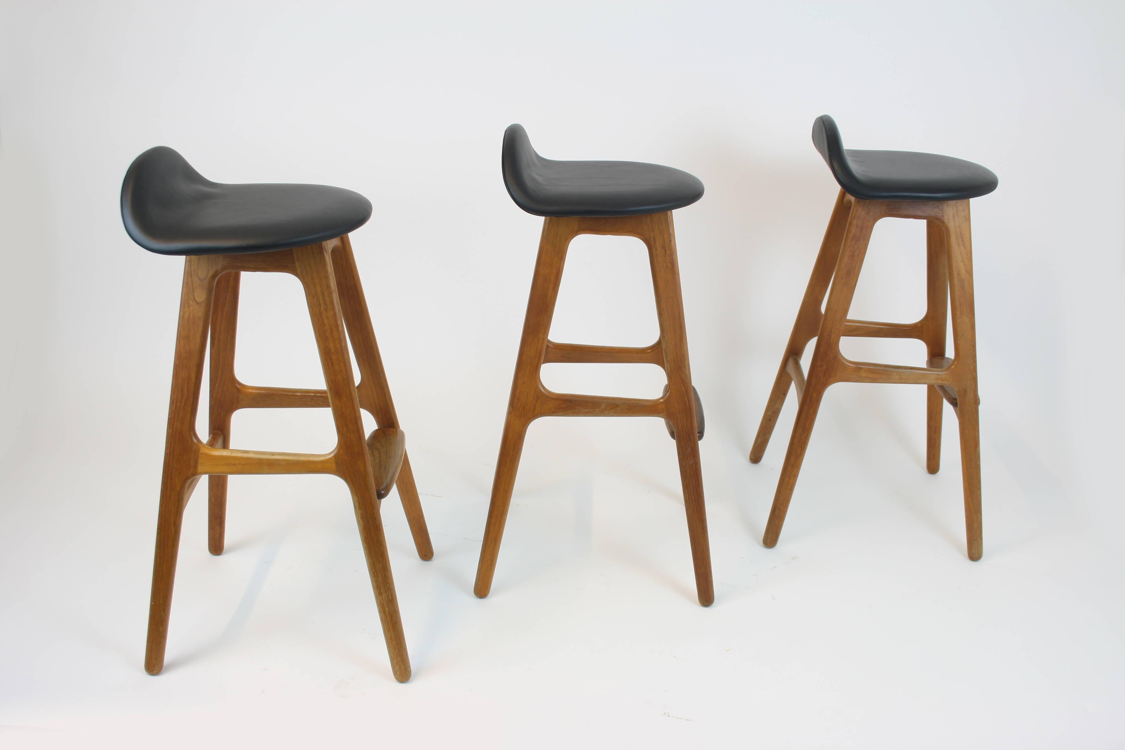 Three bar stools by the Danish designer Erik Buch (pronounced: Buck), manufactured by the Odense furniture factory in the late 1950s. Our variant of the stool is made of solid teak wood and its seating newly upholstered with black leather. Their