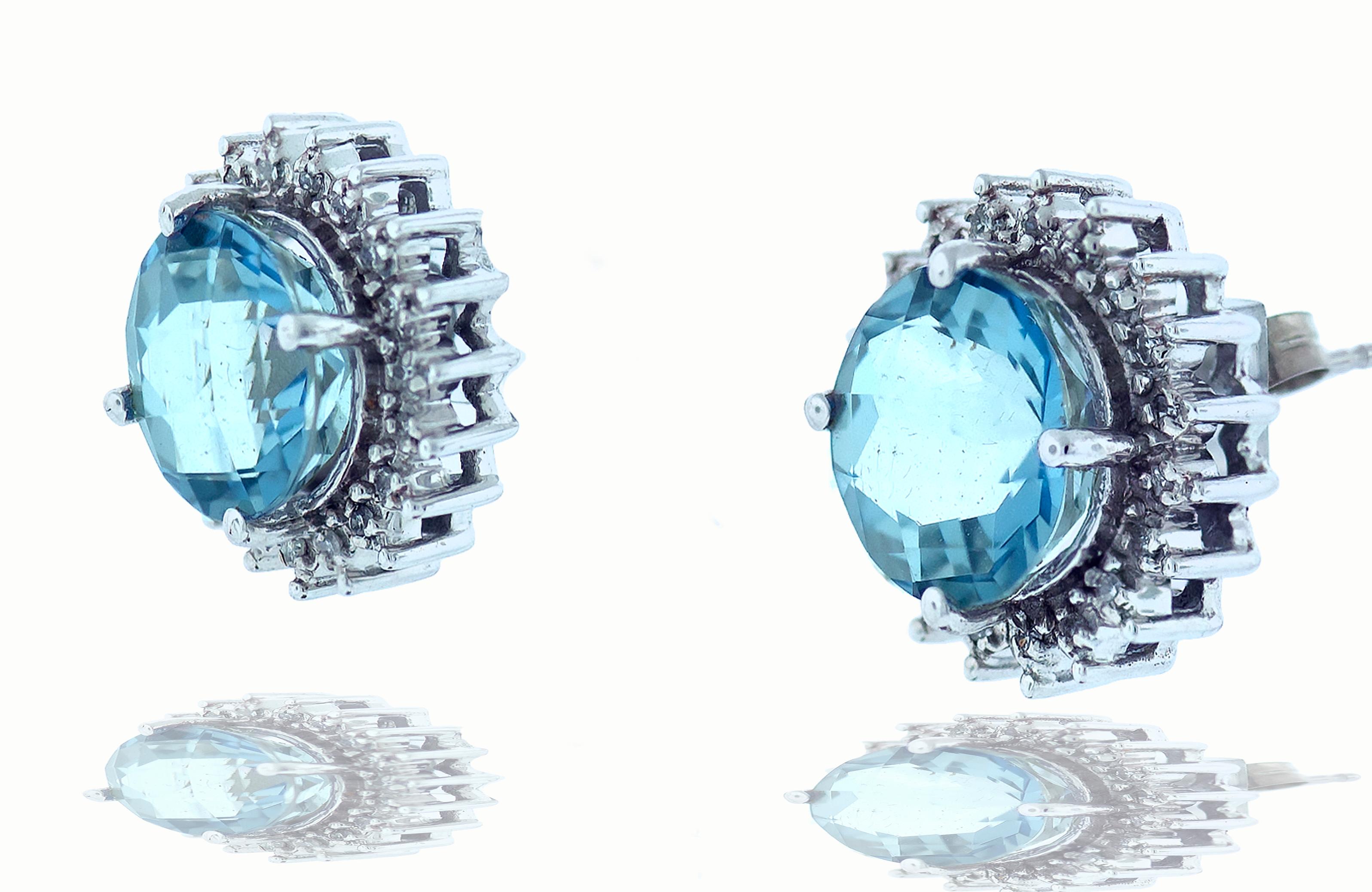 A set of blue topaz earrings with diamond halo. Each earring is set with a blue topaz that measures 9.77mm by 9.85mm that is approximately 3.3 carats.  The topaz stone earring includes a diamond halo surrounding the center stone. There are 19, 1mm
