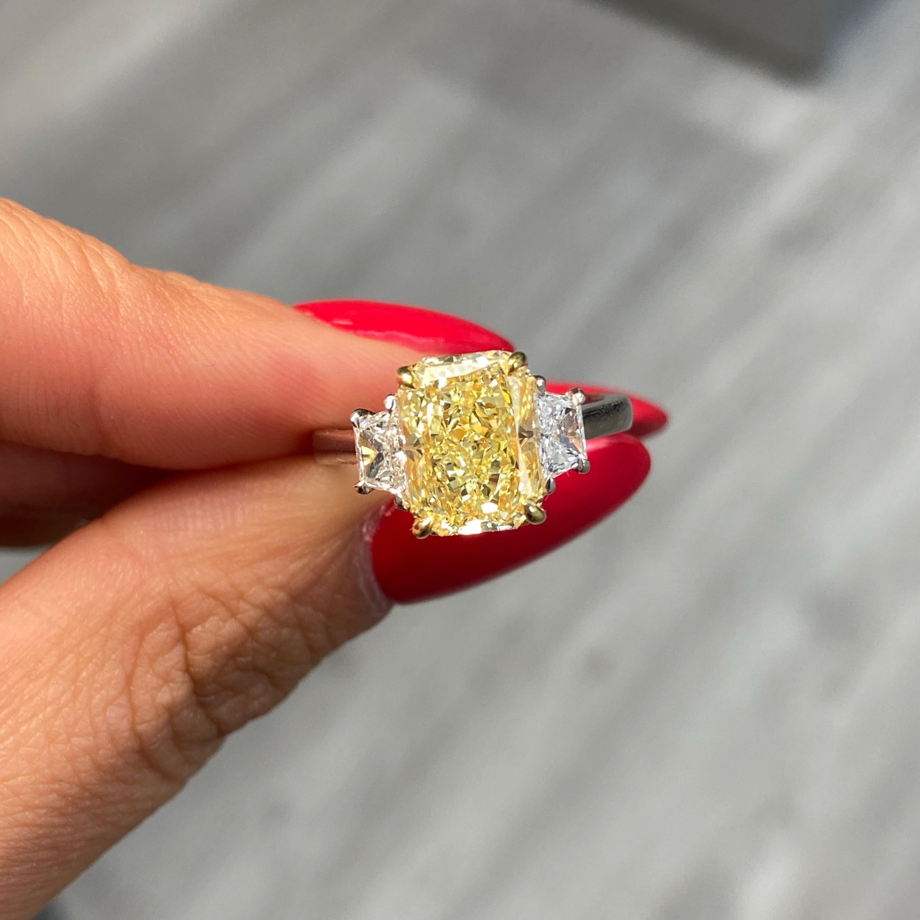 Ein zeitloser Klassiker mit einer lebendigen Note: Im Mittelpunkt dieses Verlobungsrings mit drei Steinen steht ein 3,02 Karat schwerer Fancy Yellow-Diamant im länglichen Radiant-Schliff, der für seine eleganten Proportionen und seine lebendige