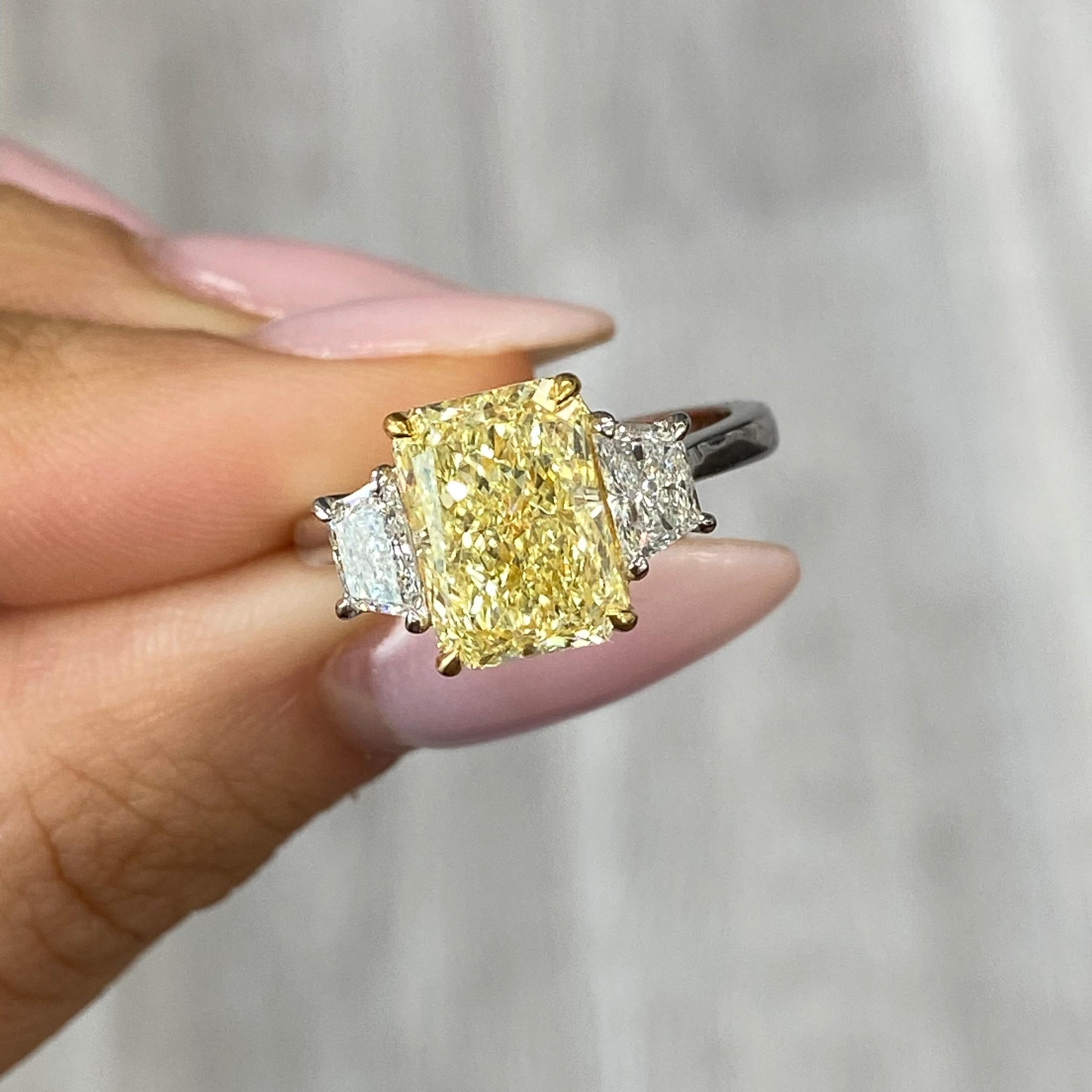 This exceptional piece showcases a stunning 3.02 carat elongated radiant cut Fancy Light Yellow diamond, graded VS2 clarity with excellent cutting for brilliance. Framed by 0.55 carat D VS1 trapezoid side diamonds, this ring is a true masterpiece.