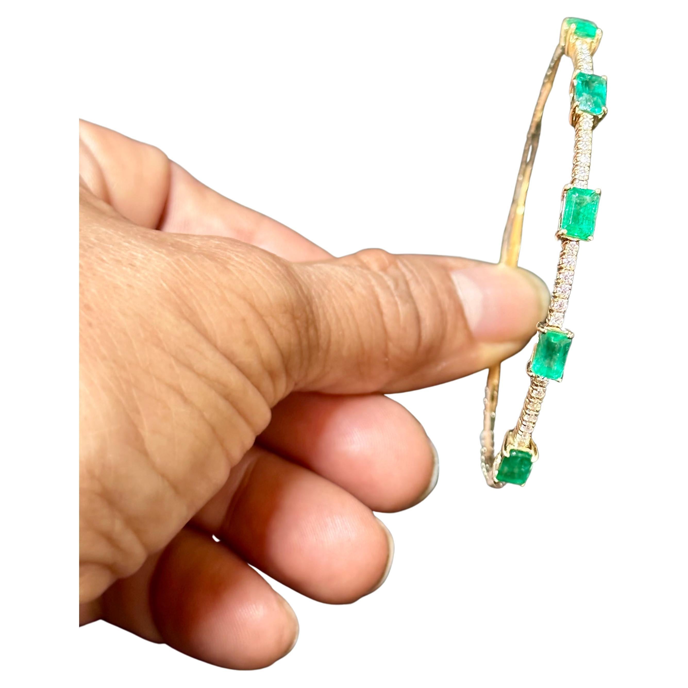 Introducing our exquisite 14 Karat Yellow Gold Bangle Bracelet adorned with approximately 3 carats of Natural Brazilian Emeralds and sparkling diamonds. This bangle bracelet showcases five emerald-cut emeralds, each meticulously separated by a row