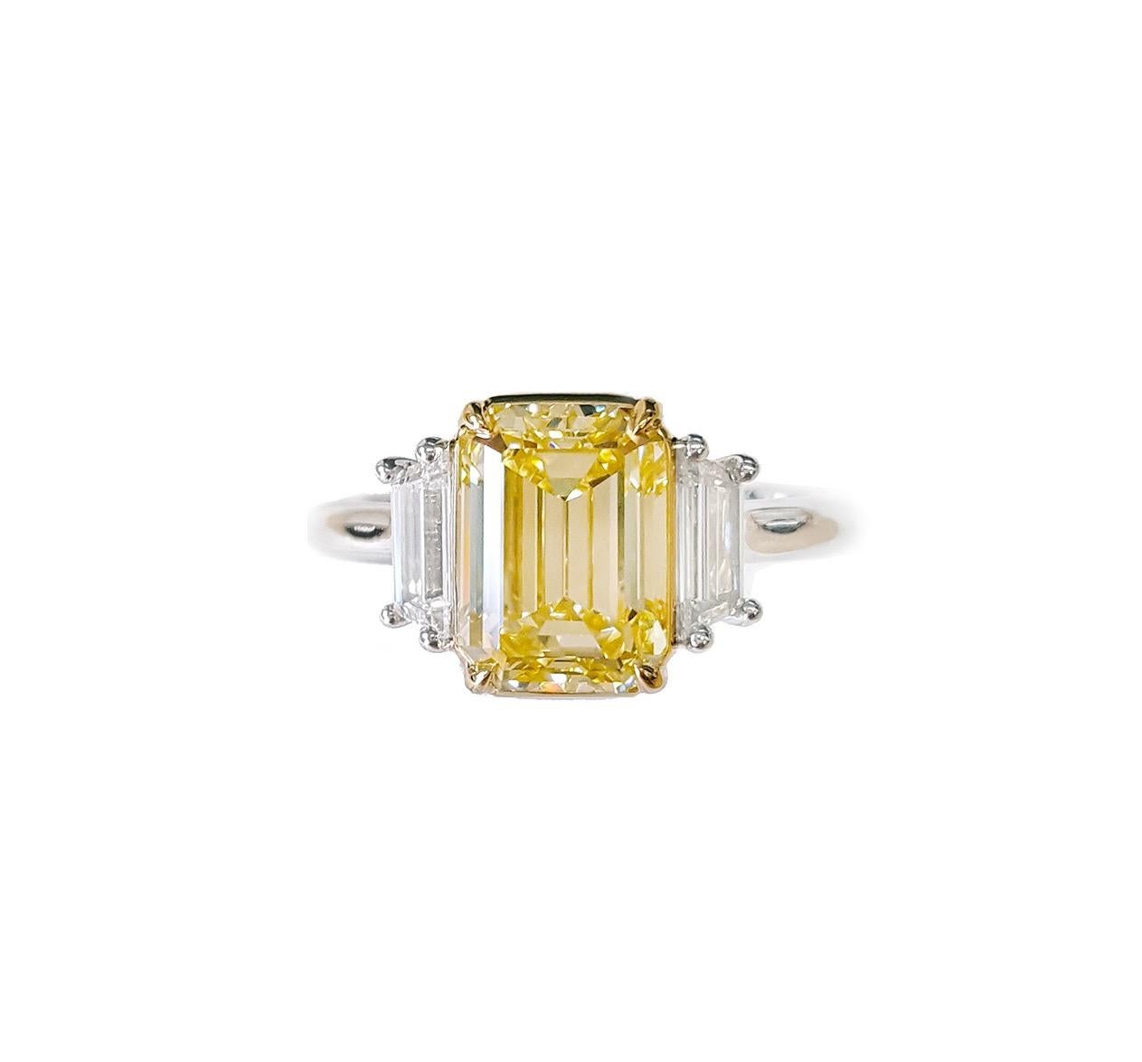 Presentamos un impresionante Anillo de Compromiso de Tres Piedras que luce un deslumbrante 3 quilates  Diamante amarillo talla esmeralda. Certificado GIA como claridad VS1. El diamante central está bellamente complementado por dos diamantes de talla