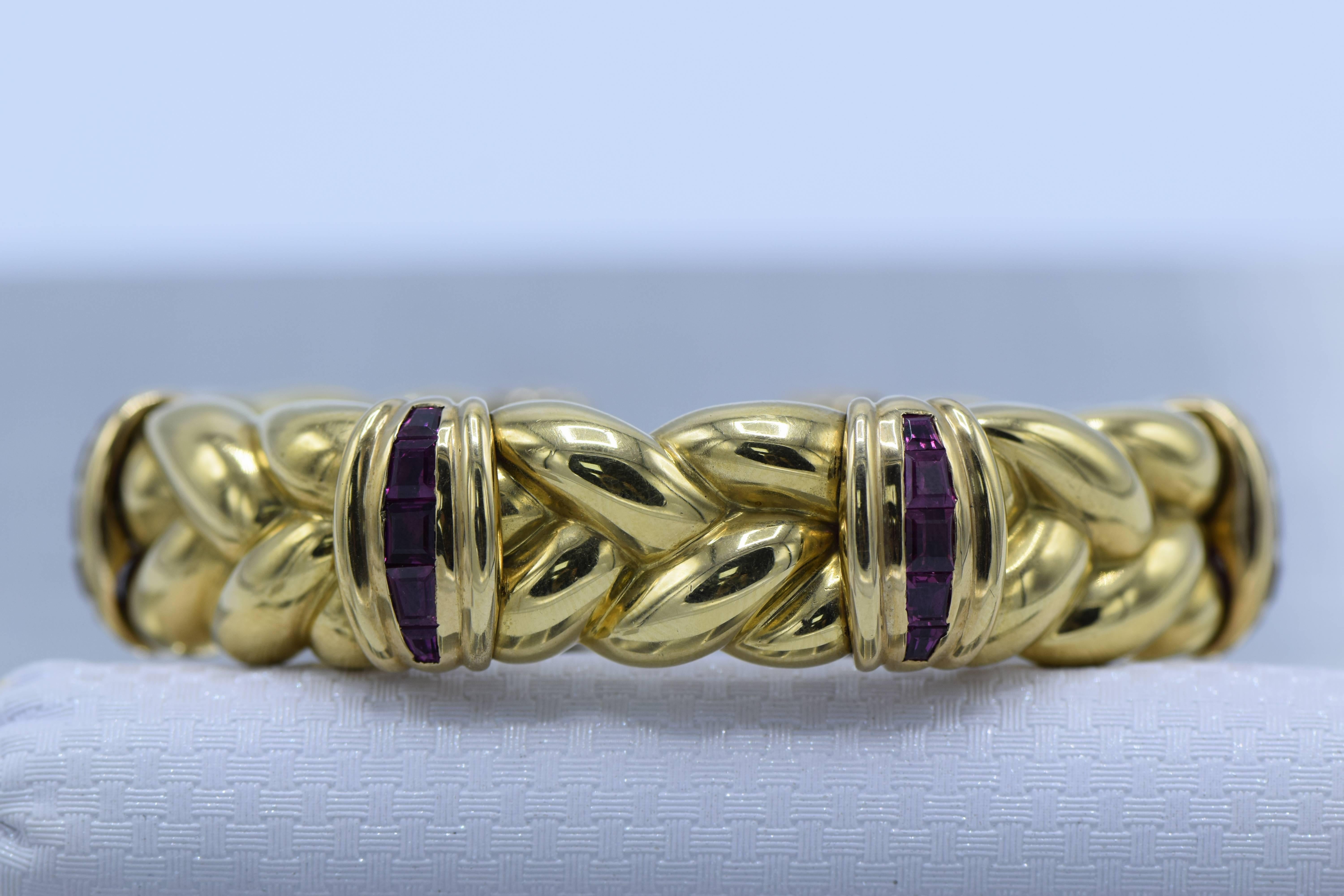 The penannular slightly spring-mounted braid motif with a quartet of fluted stations accented by channels of rubies, in 18k gold, inner circumference 6 1/8 inches

Dimensions: 16 mm 

Rubies: medium dark pinkish red