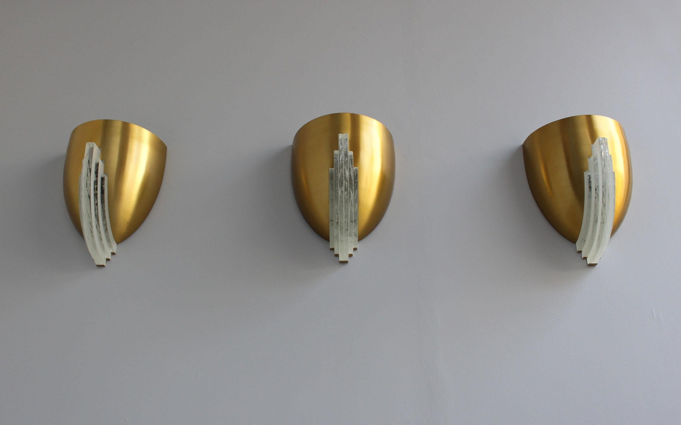 Jean Perzel - Tre raffinate applique francesi Art Déco realizzate con una coppa semi-ovale in bronzo ornata da lastre di vetro cristallino. 
Firmato.
Il prezzo si intende per applique