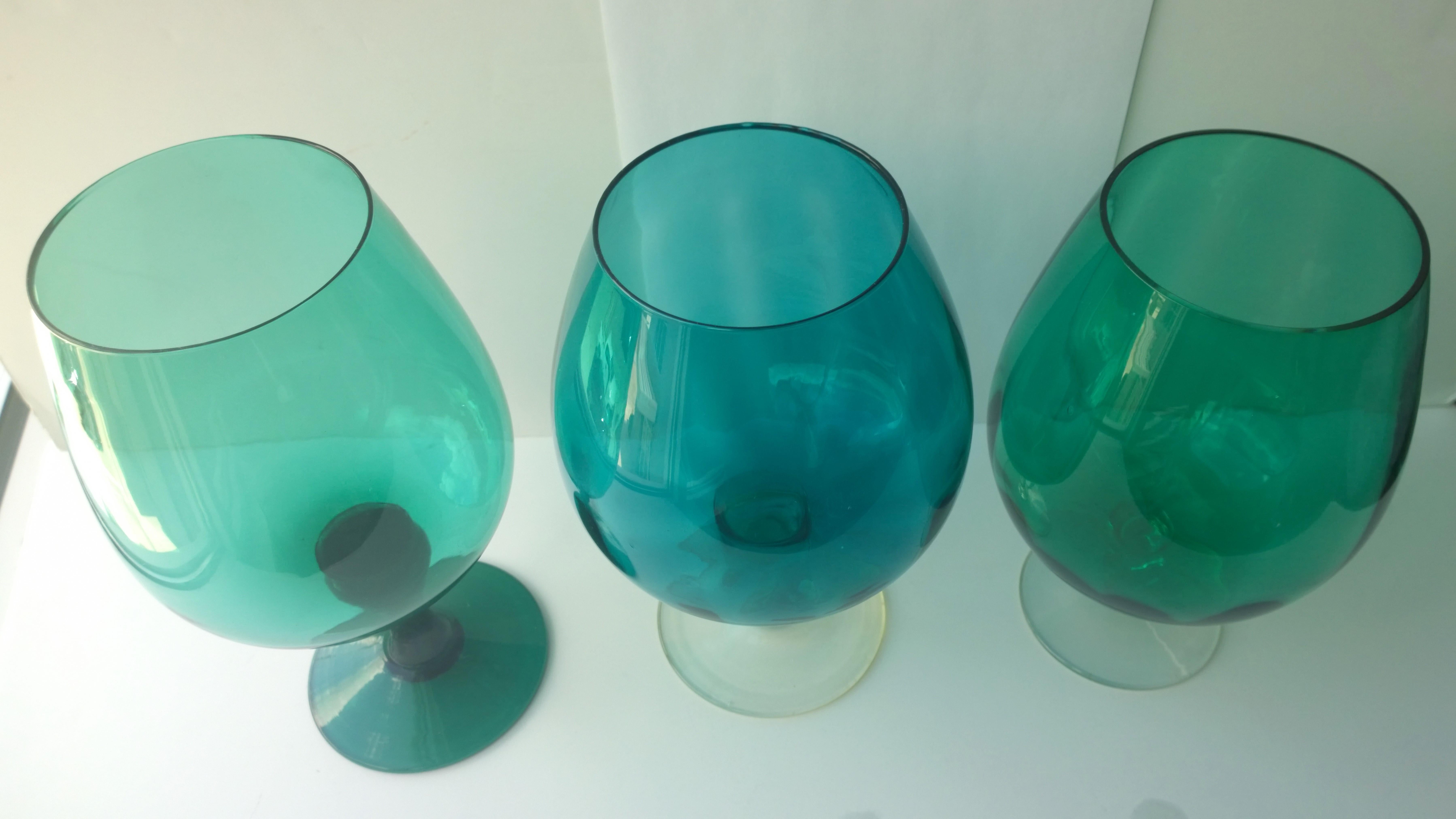 Offered are three Mid-Century Modern hand blown oversized brandy snifters or vases in emerald, teal, peridot (Sold) and Monterey bay green glass with clear glass stems. Would look great as decor, with flowers or on a bar or bar cart. Can be