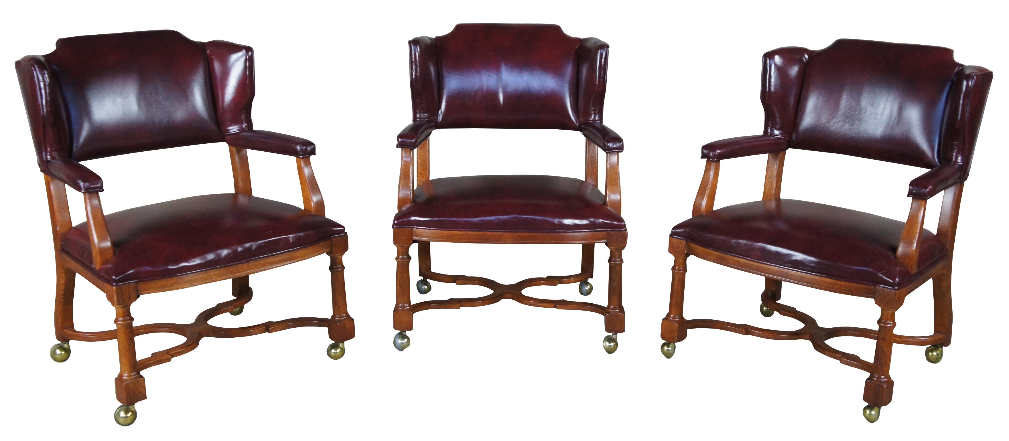 An exquisite trio of mid century wingback office, game or dining chairs by Hickory Manufacturing Company. Executive styling with oak frame upholstered in a red burgundy leather. Features padded arms, turned legs and a Tuscan inspired H stretcher.