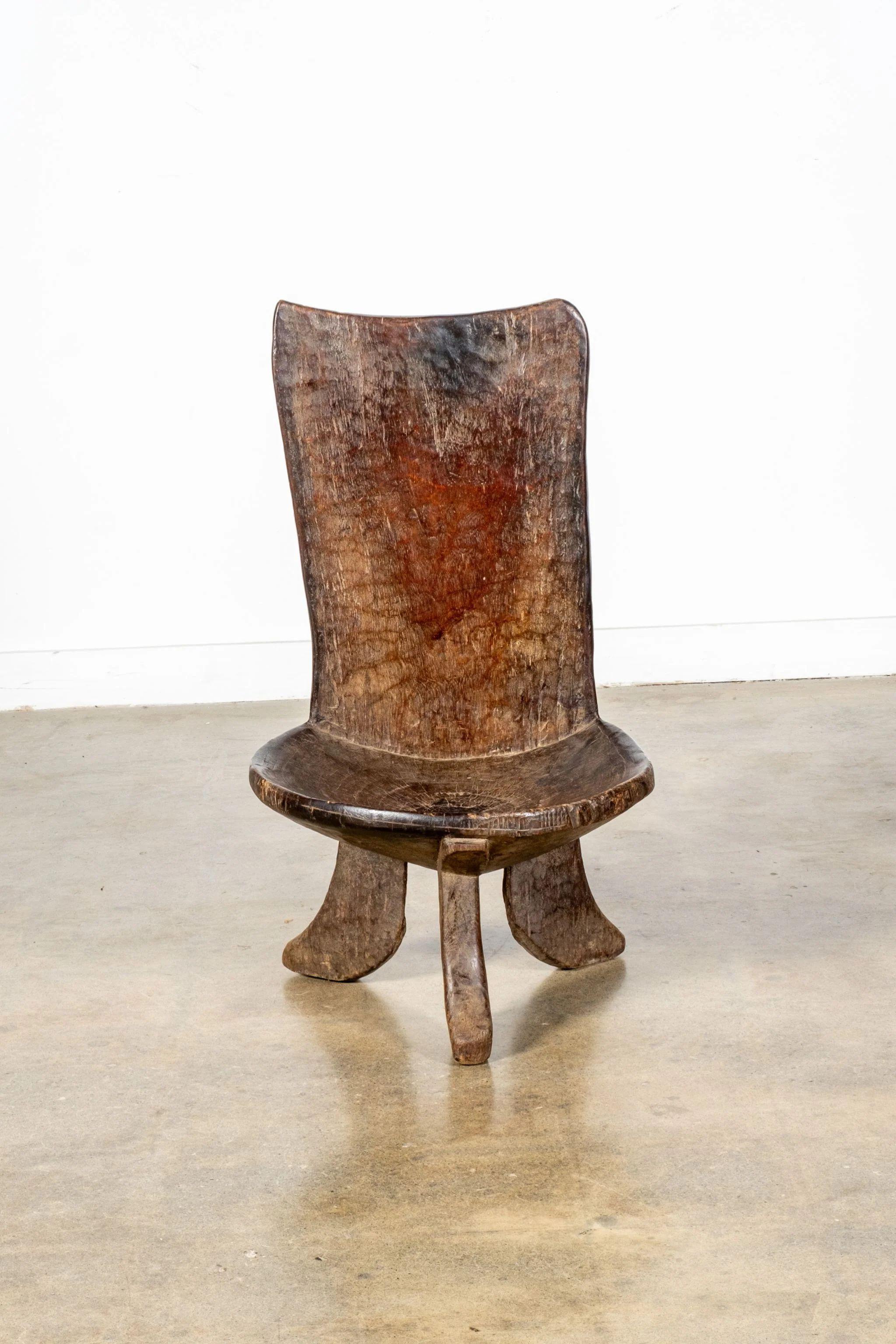 Three-legged African chair, dating from the first half of the twentieth century, made of black patinated hardwood. The round slightly-hollowed seat contrasts with the square carved backrest, carvings adorn the flat back of the seat, while a