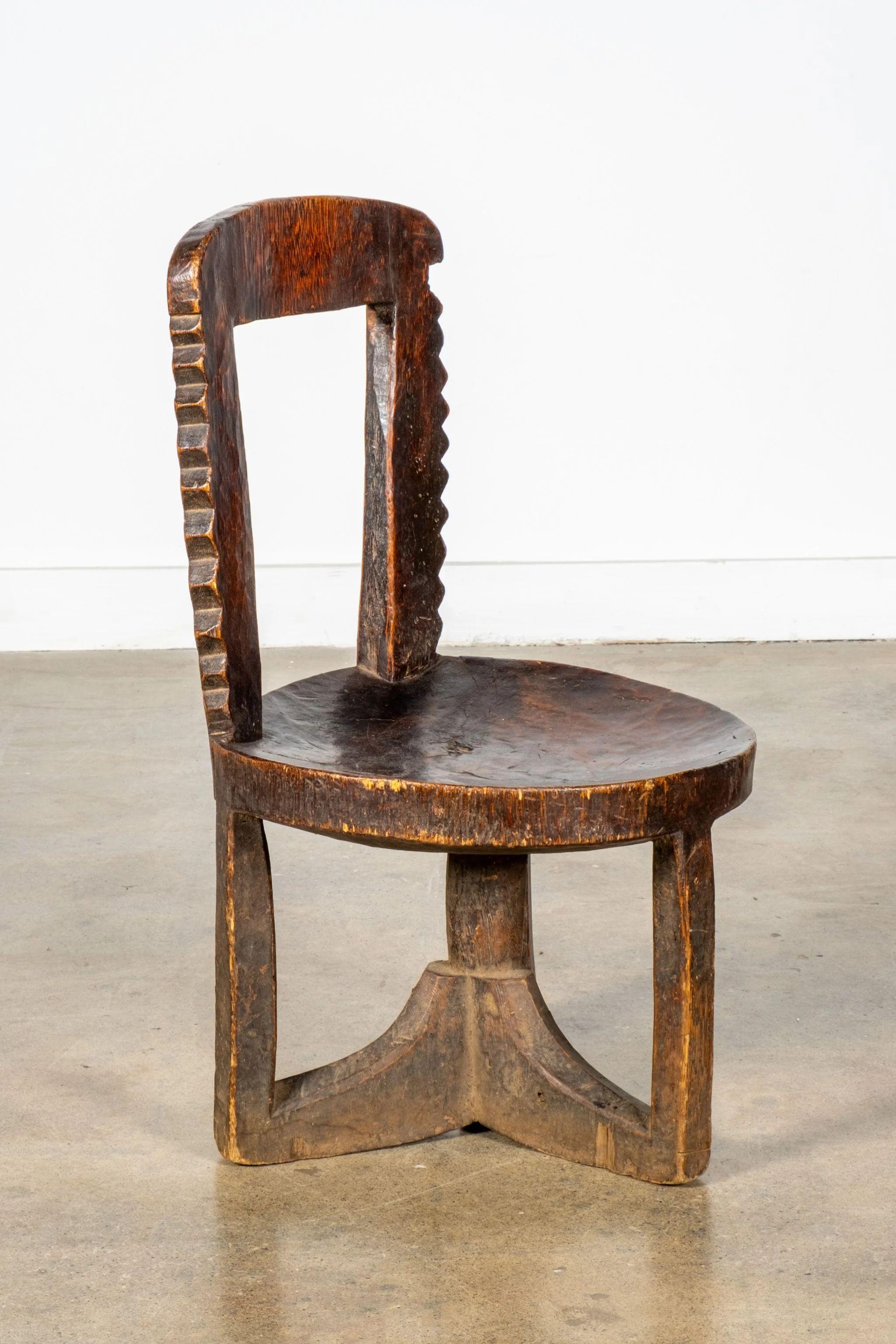 Three-legged East African chair, dating from the first half of the twentieth century, made of black patinated hardwood. The round slightly-hollowed seat complements the squared-off carved scallop windowpane back, while a weathered look unifies the