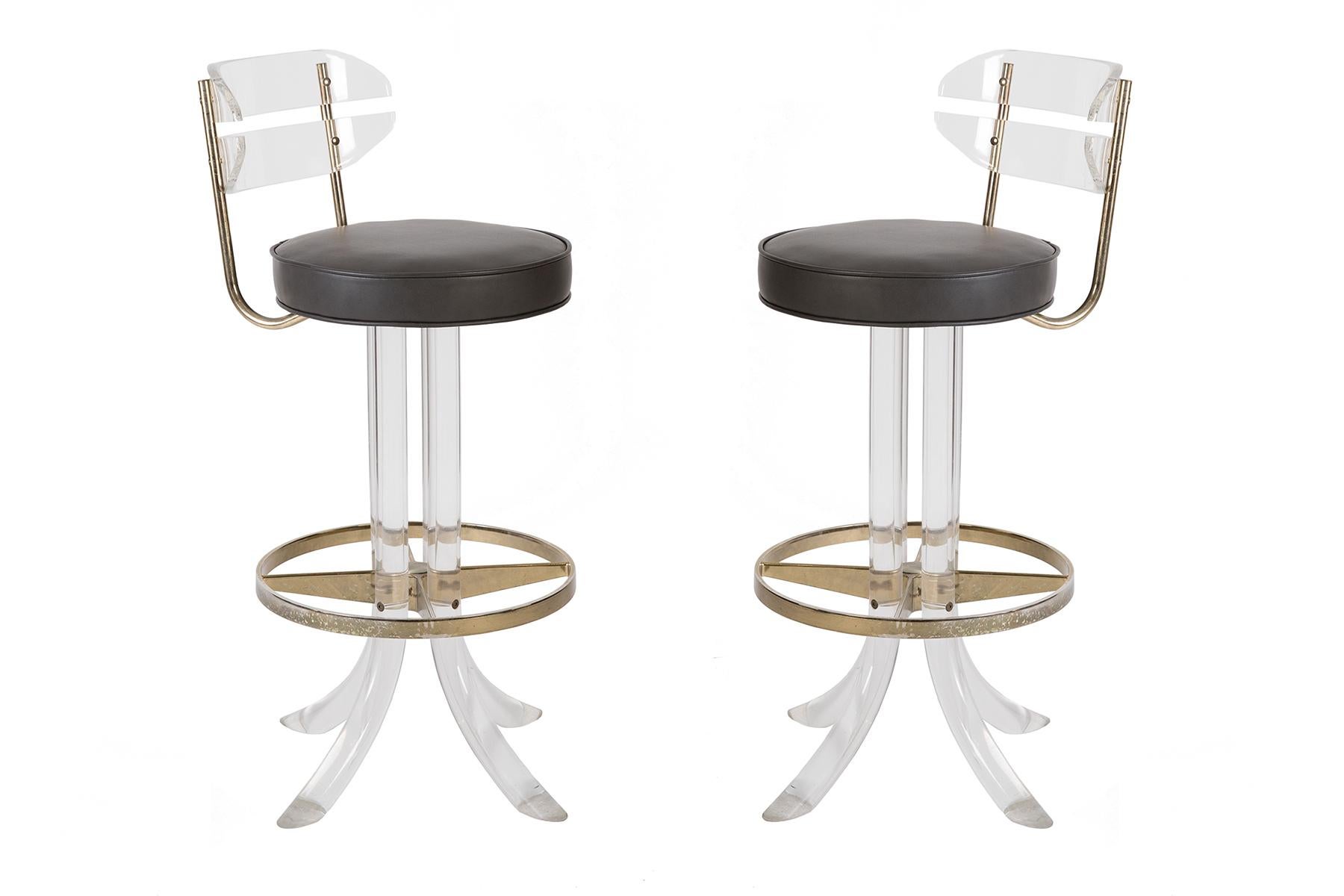 3 barstools with a fantastic mix of materials--conveying a modern lightness with clear Lucite on the legs and backs, flanked by futuristic touches of brass and a supple dark grey leather seat. Each stool has newly upholstered seats and swivels so