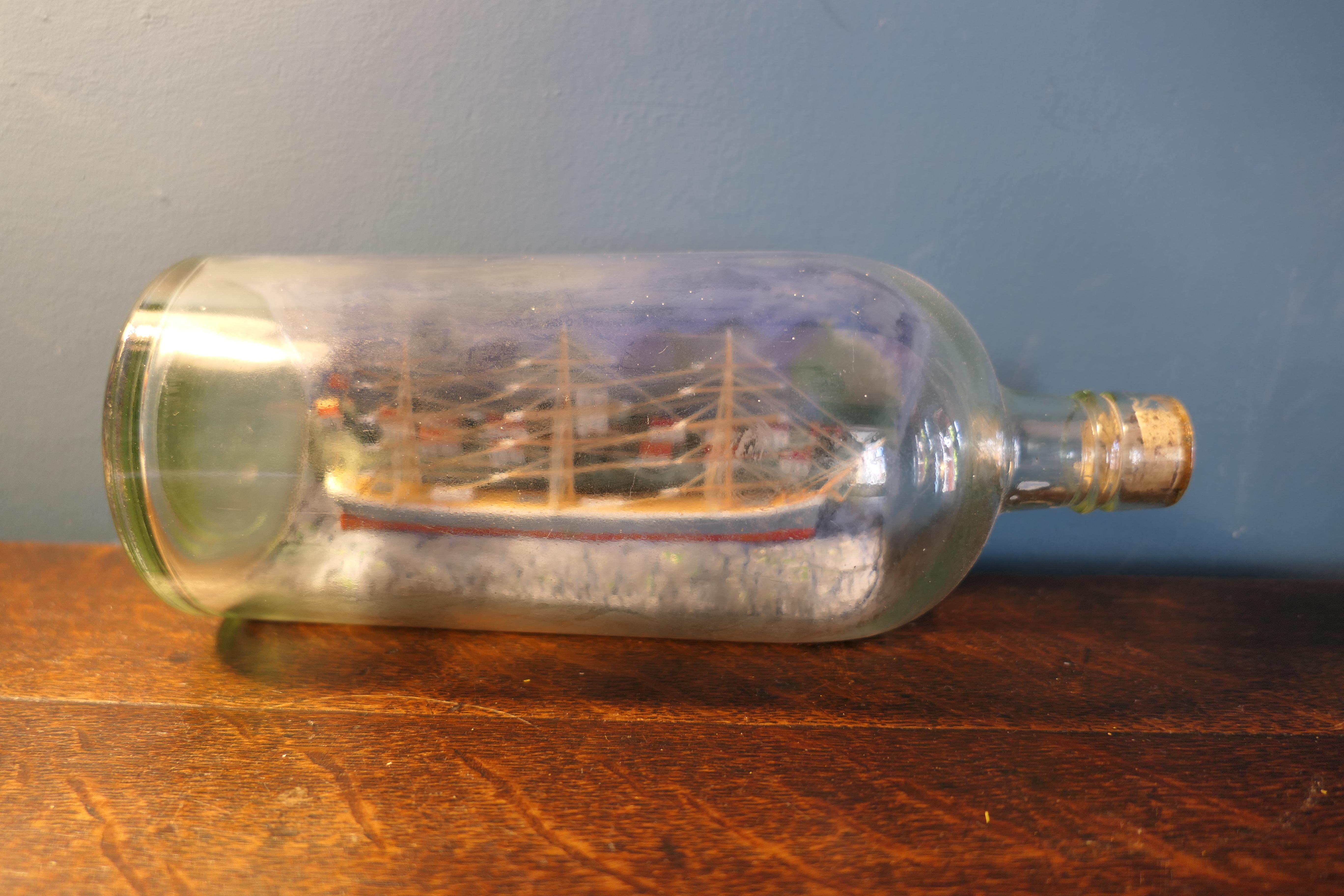 Un voilier à 3 mâts dans une bouteille 

Diorama détaillé d'un modèle de bateau dans une bouteille d'alcool datant d'environ 1920. 
Il représente un voilier en bois à trois mâts entièrement gréé dans un port de Cornouailles, avec une finition