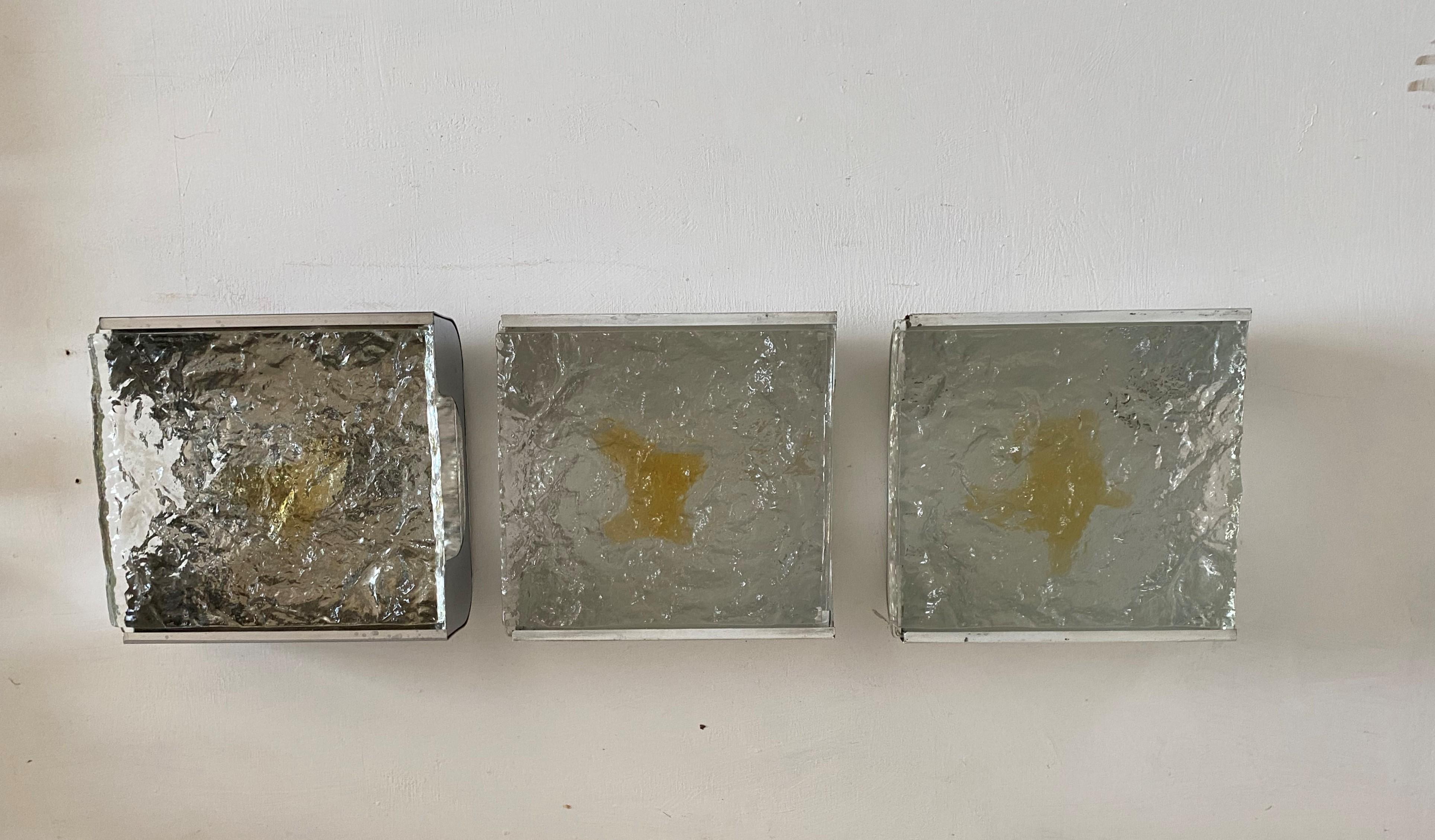 3 Mid-Century Modern Murano glass sconces manufctured by Venini, circa 1960, in clear and amber thick Murano glass slabs.
Metal hardware lacquered white.
It is shown with warm and cold bulbs so the difference can be appreciated.
We have several