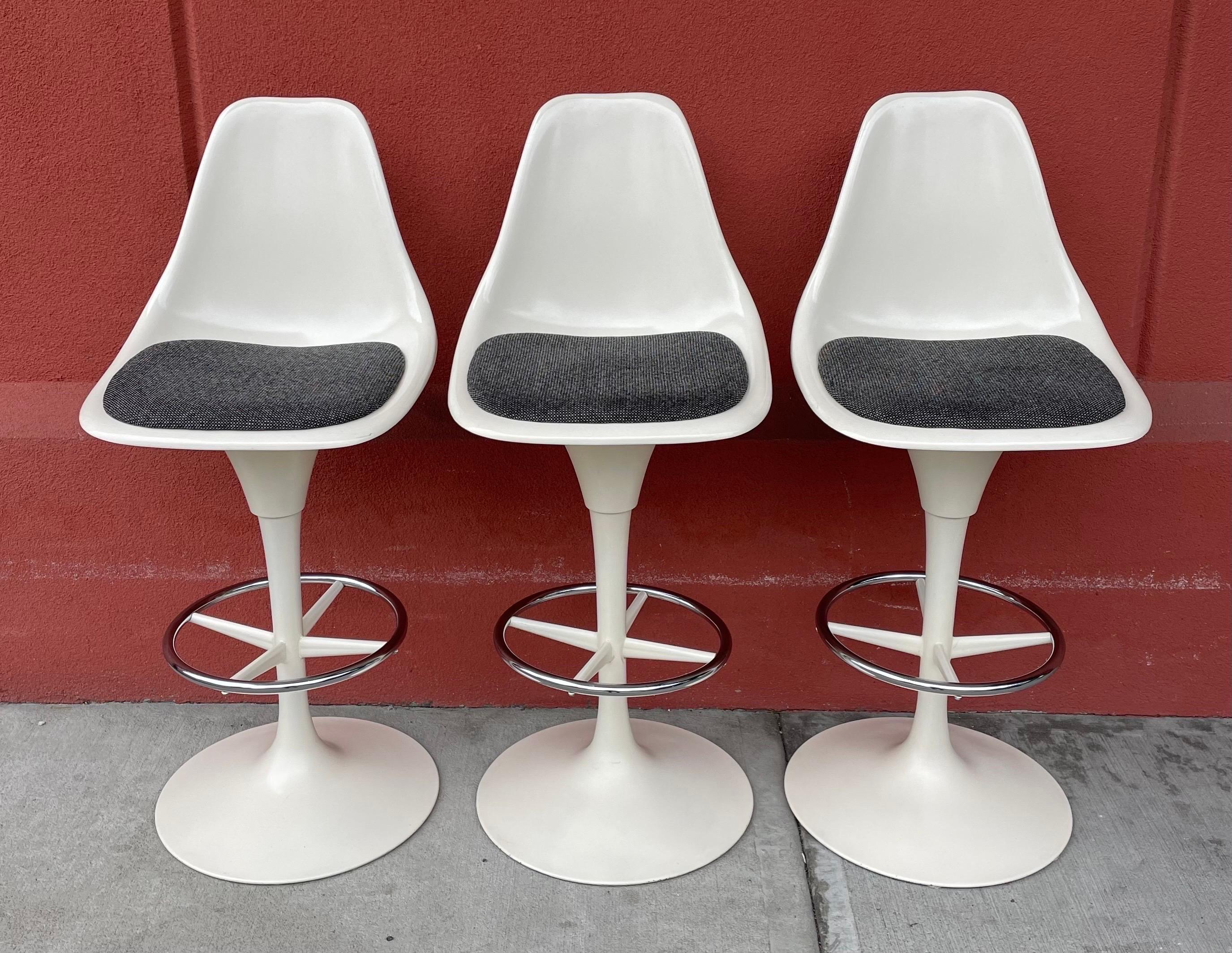 Very cool, rare and authentic mid century swivel bar stools in the style of Eero Saarinen for Knoll. Bar height, swivel seat, white metal tulip base, footrest, molded fiberglass seat with slim dark gray seat cushion. All original condition with