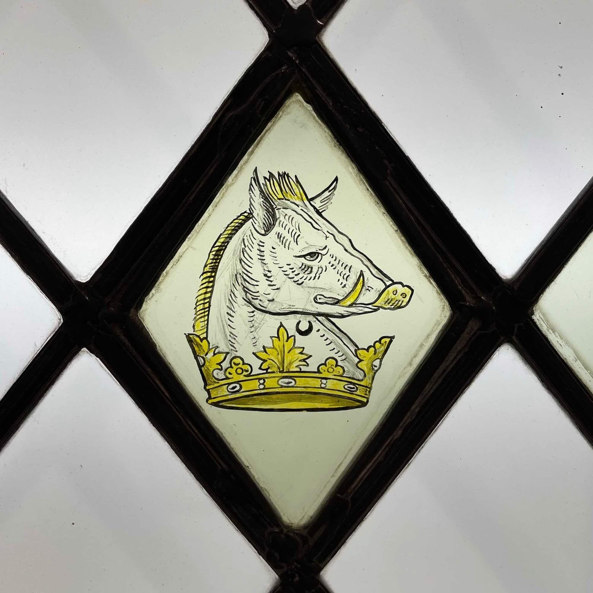 A 3 pane antique leaded glass window detailed with hand painted heraldic symbols: a boar, a portcullis and a coat of arms reading ‘Honi soit qui mal y pense’ (translating to ‘shame on him who thinks evil of it’), motto of the Order of the