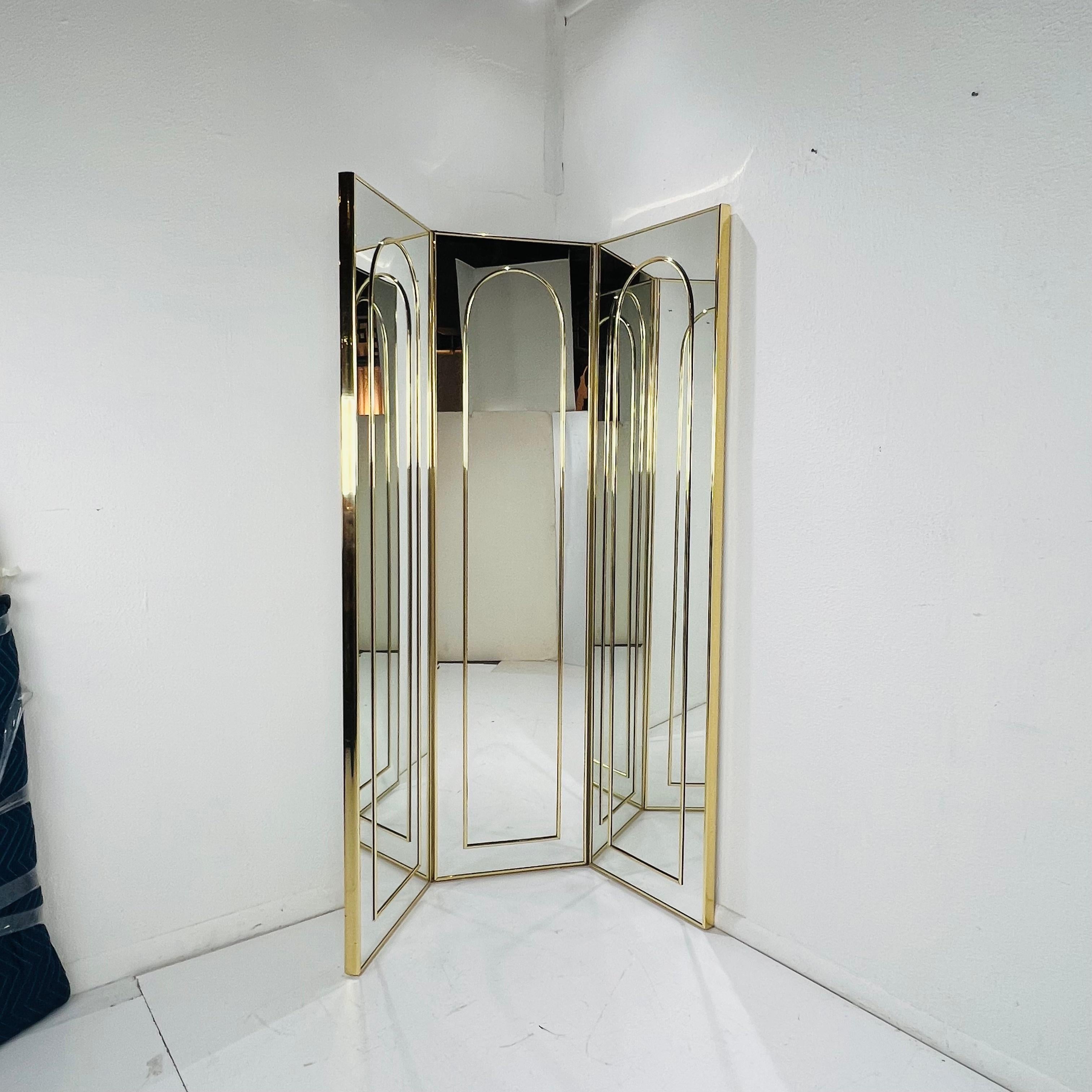 Mid century mirrored screen / room divider. The three panels are mirrored front and back, with the front side featuring brass arches. Panels meet at top and bottom hinges to stand independently. Minimal age-related wear, very good condition.