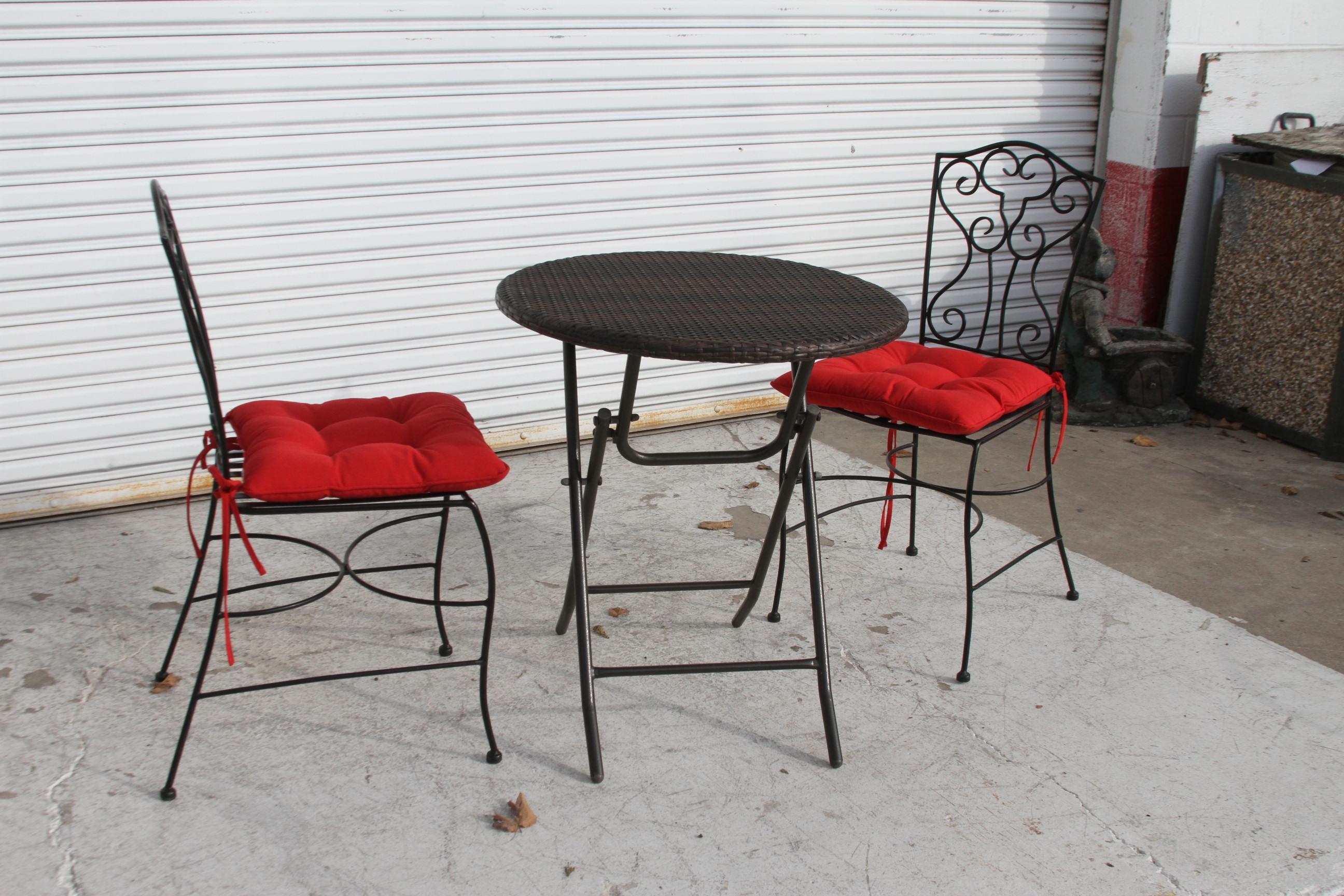 Il s'agit d'un mignon petit ensemble de bistro boho chic. Le plateau de la table est en rotin tressé sur un cadre métallique. Les chaises sont en métal avec de beaux coussins rouges pour le confort. Les dossiers des chaises sont conçus. 

Les
