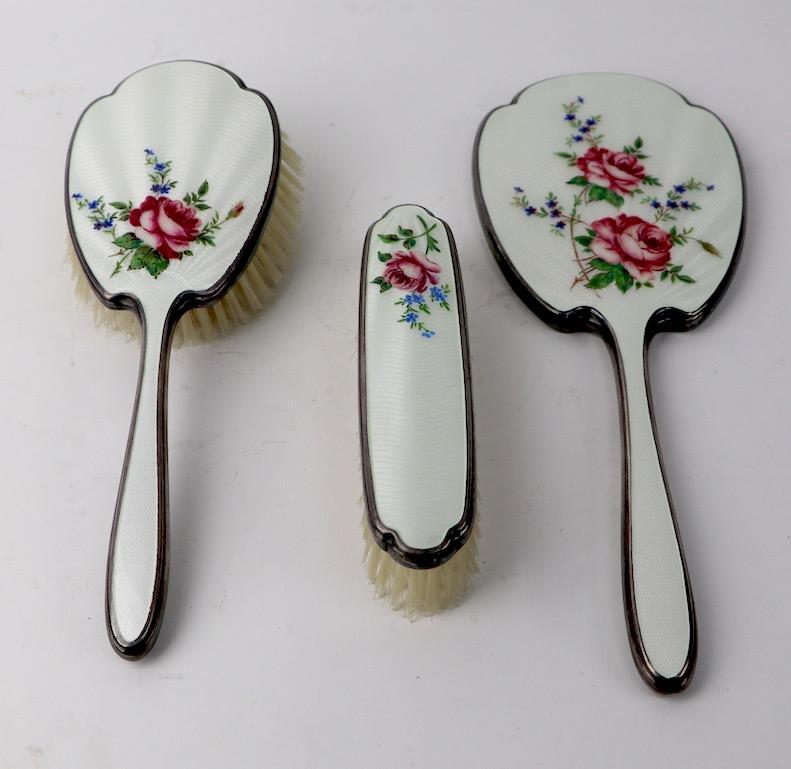 Sweet and charming 3-piece. Enameled vanity set includes hairbrush, clothes brush and hand mirror. Set is marked Made in England, and bears makers touch marks, believed to be silver, attributed to W. G. Sothers. Free of damage, wear or condition