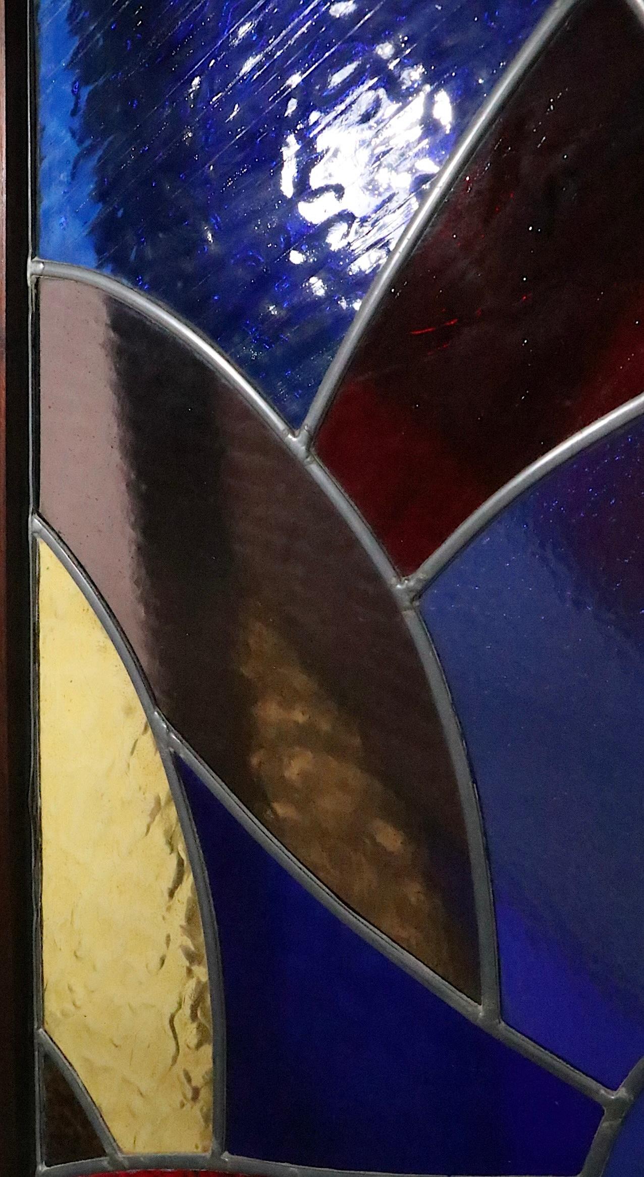 Ensemble inhabituel de trois panneaux de vitrail au plomb, exécutés dans le style moderniste, constitués de pièces de verre coloré, fusionnées avec des garnitures en plomb, encadrées d'une bordure en bois massif. 
 Les deux panneaux les plus grands