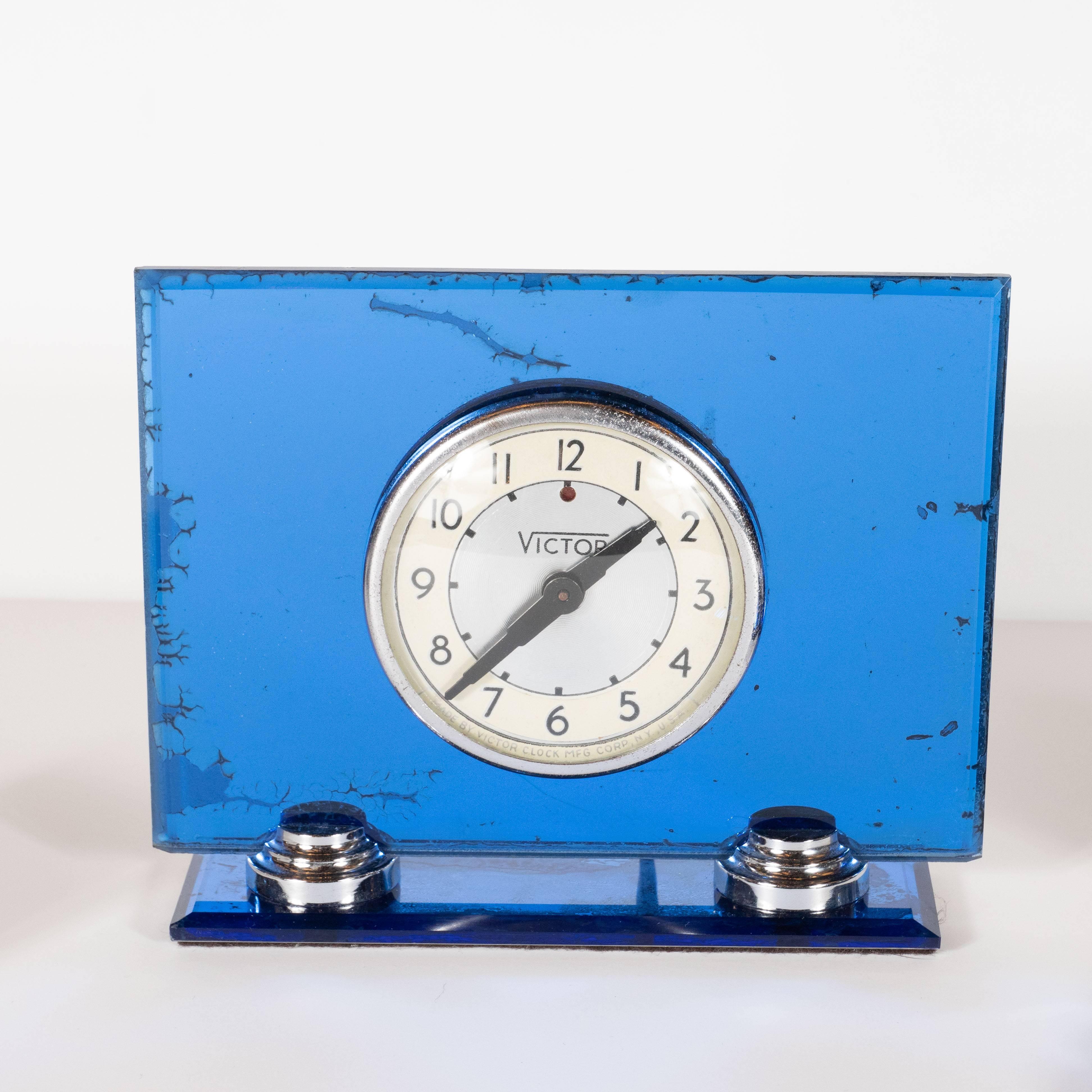 This sophisticated Art Deco Machine Age desk set was realized by the celebrated American maker, Victor, circa 1930. It features a inkwell/pen holder, a blotter and a clock. The inkwell offers a square body composed of translucent Lucite with a