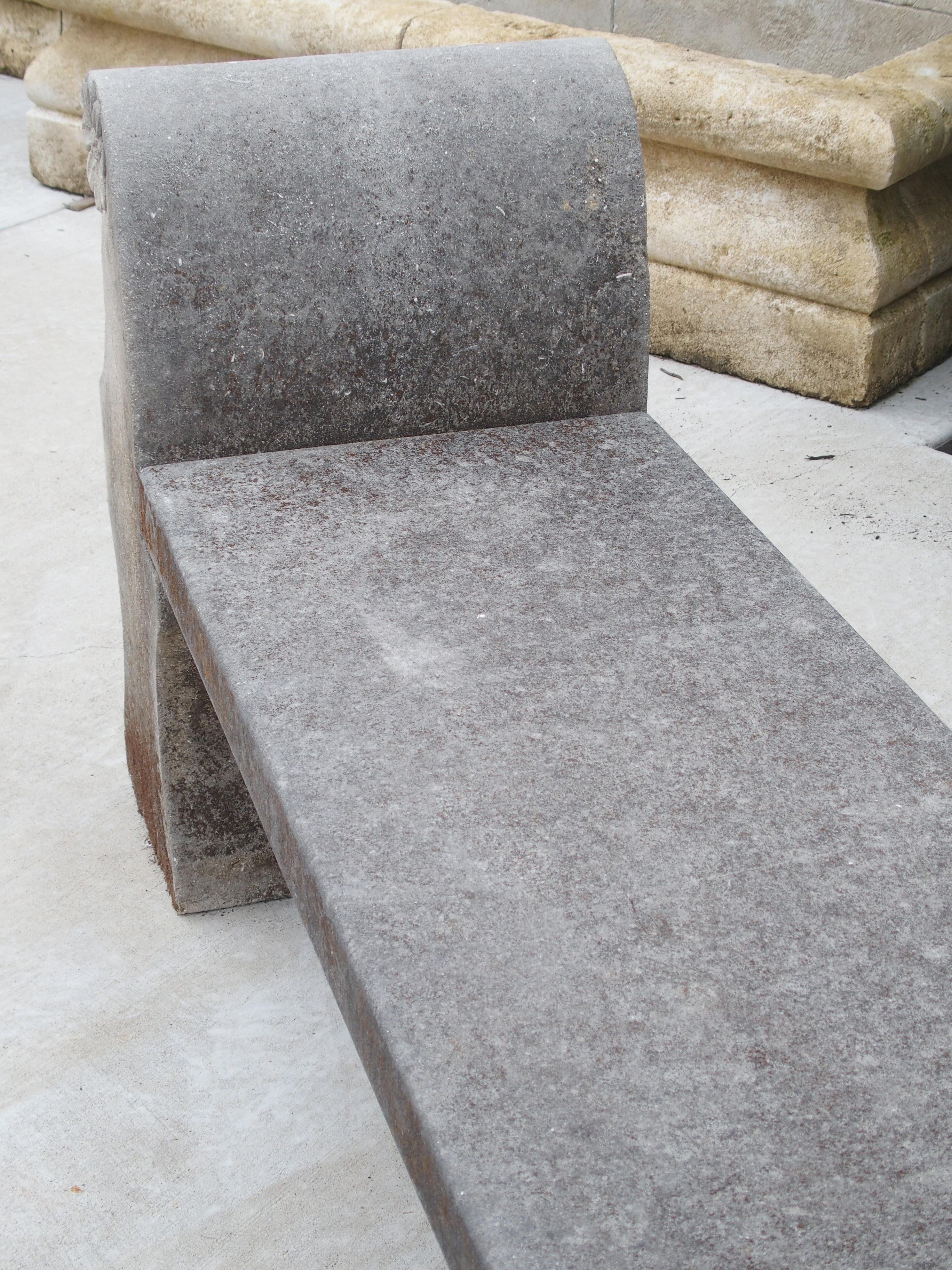 This garden bench has been hand carved from three pieces of Italian limestone. The thick rectangular seat is almost six feet long and rests on two identically shaped sides. The tops of the sides terminate in scrolled armrests embellished with carved